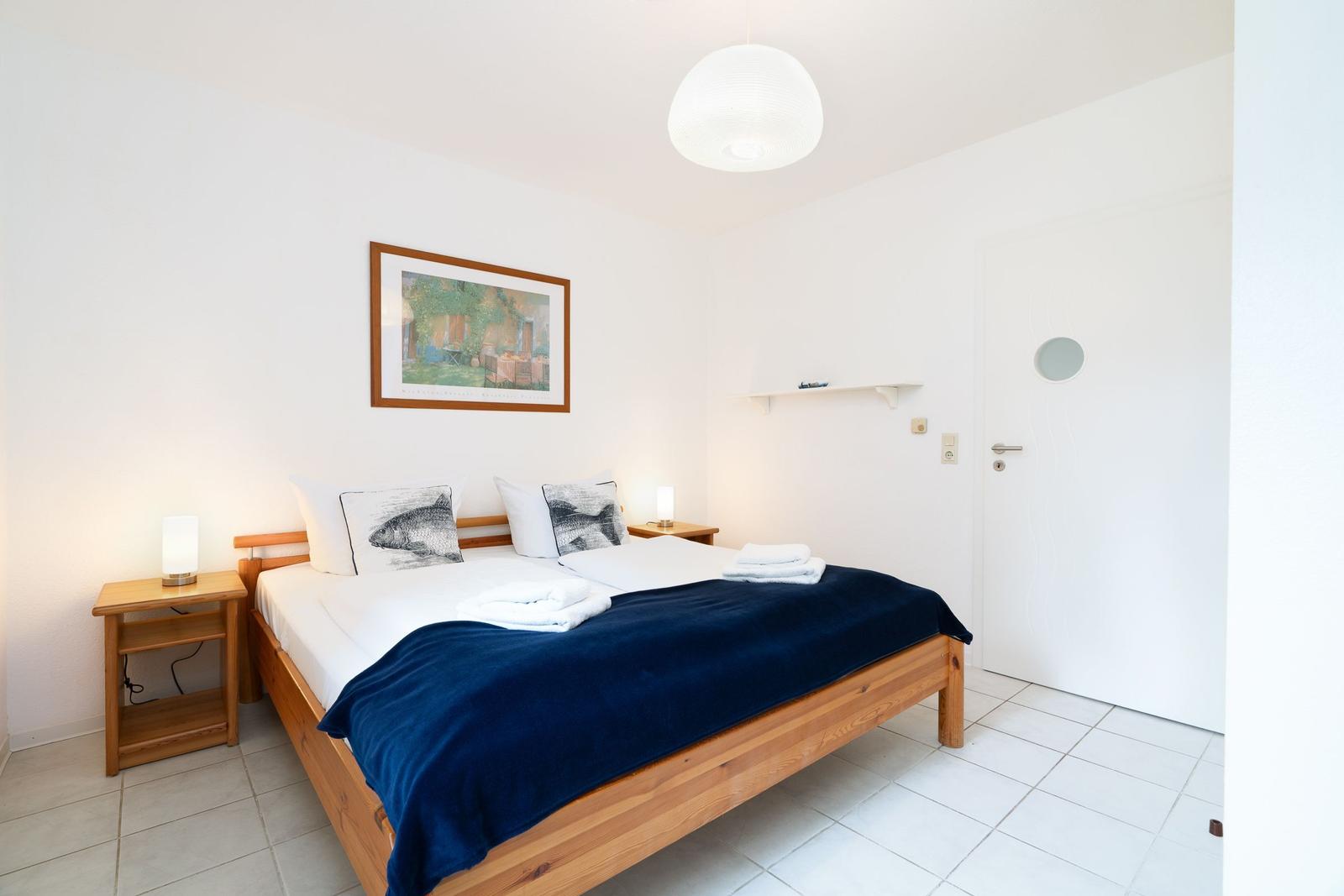 Bedroom with wooden bed, blue blanket, and nightstands with lamps.
