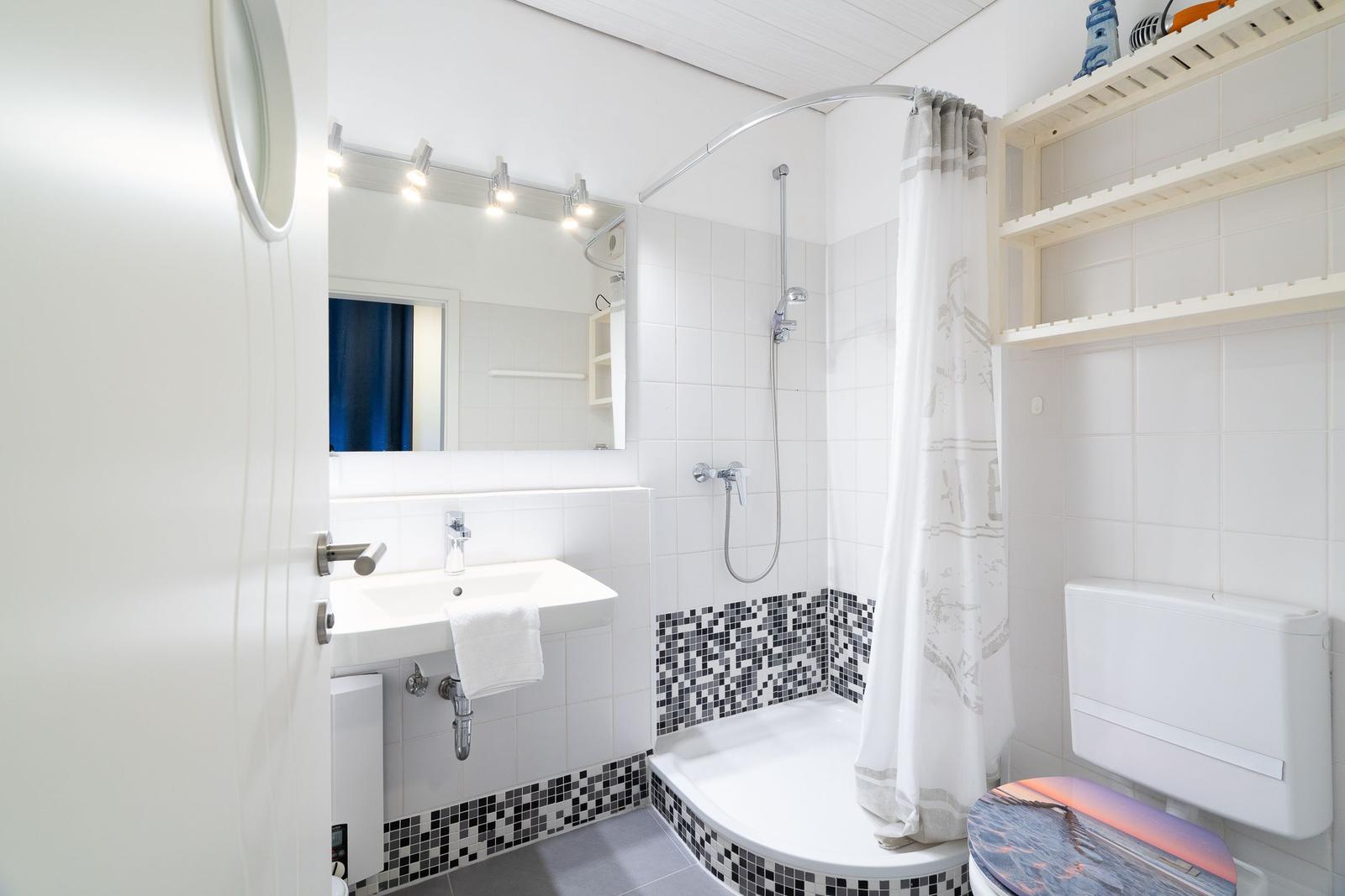 Bathroom with shower, sink, and toilet. White tiles and mosaic floor.