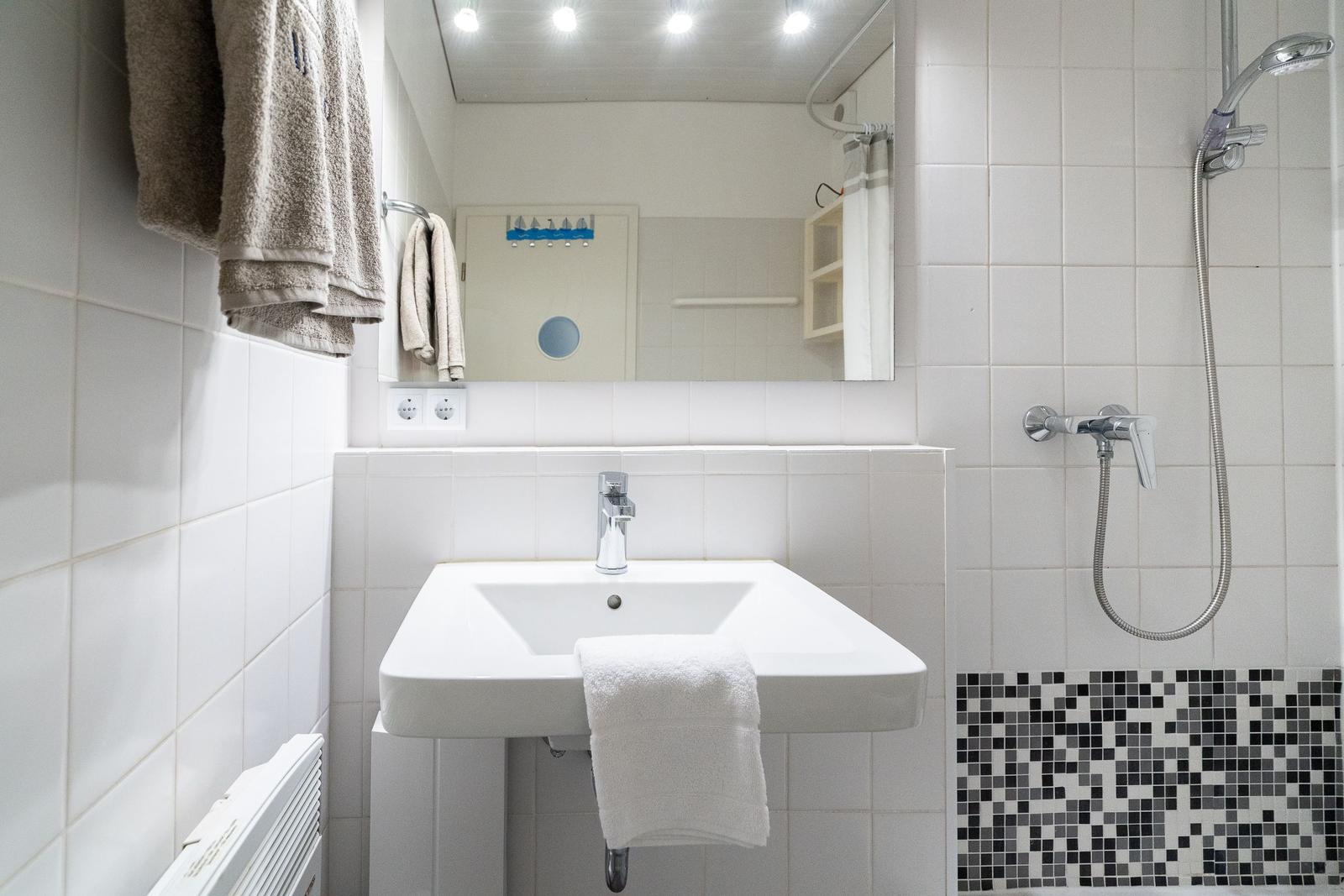 Bathroom with sink, shower, and mirror. White tiles and towel rack.