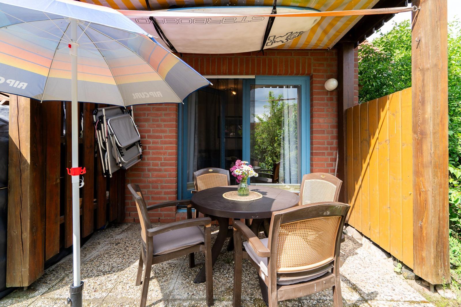 Terrace with table, chairs, and umbrella. Background: red brick wall and window.