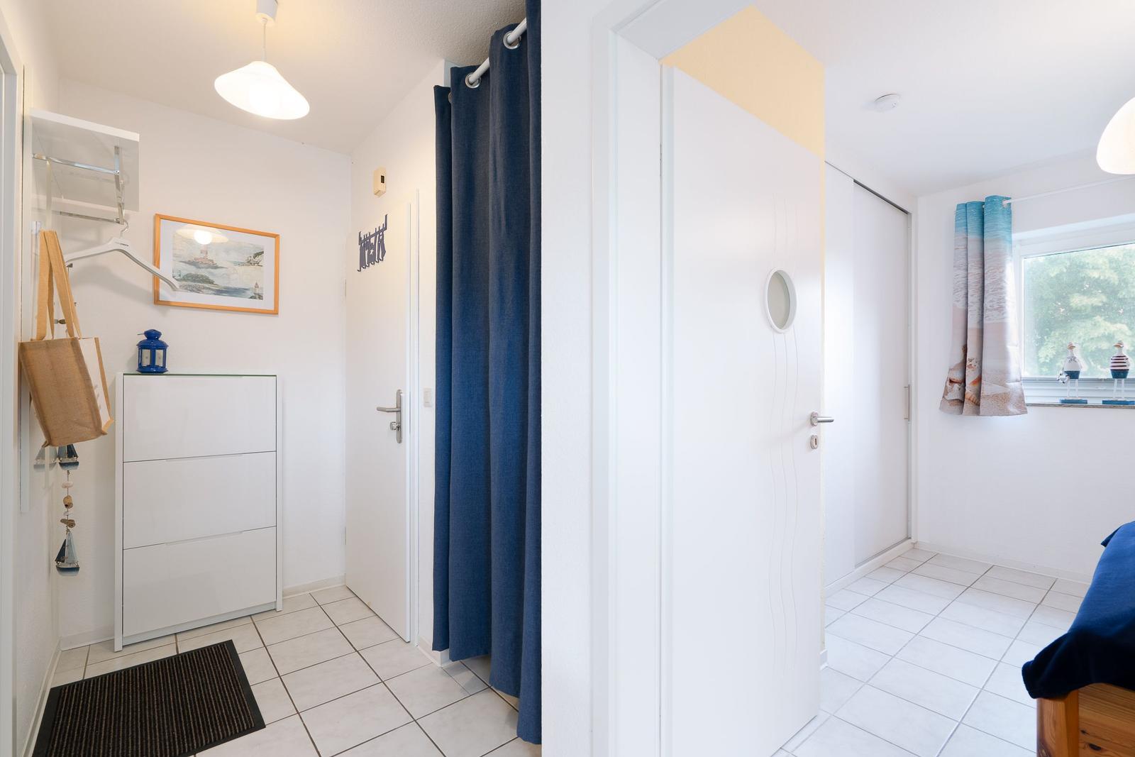 Entryway with shoe cabinet, wall picture, and curtain. View into bedroom with window and bed.