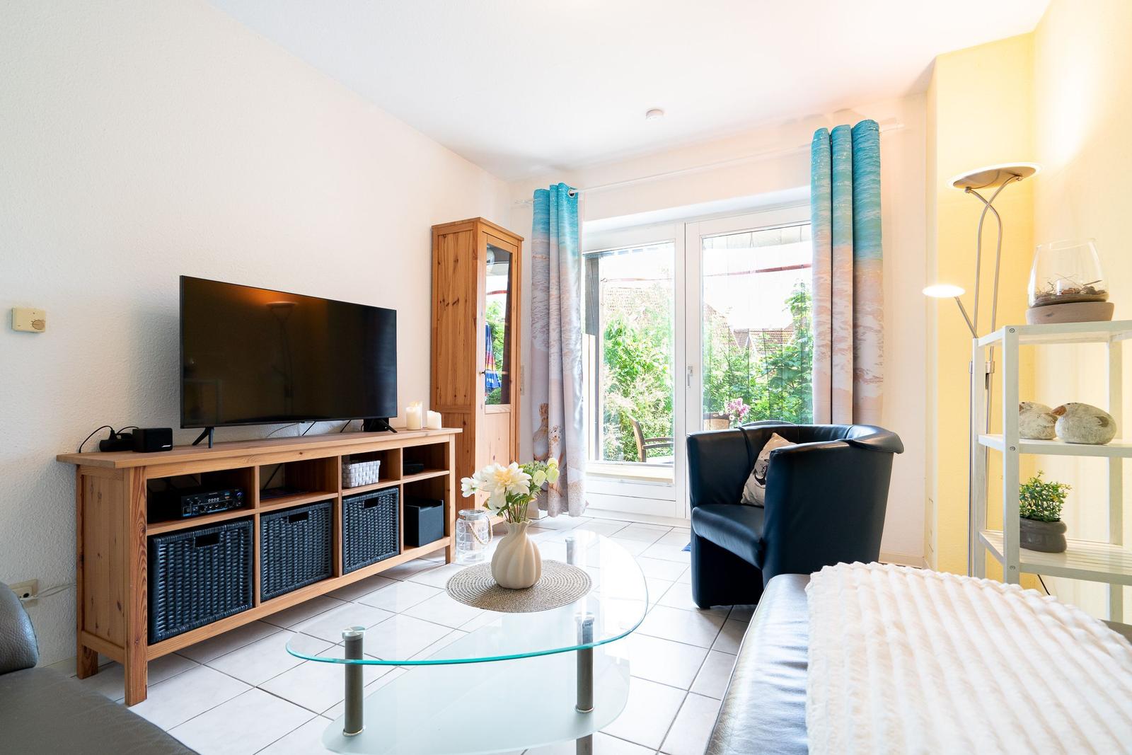 Living room with TV, sofa, and glass table. Entrance to terrace with garden view.