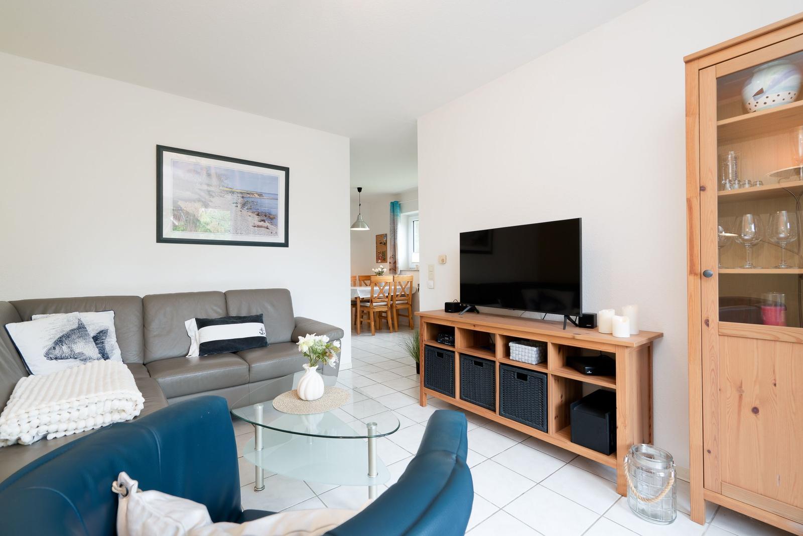 Living room with sofa, TV, and glass wall. Dining area in background.