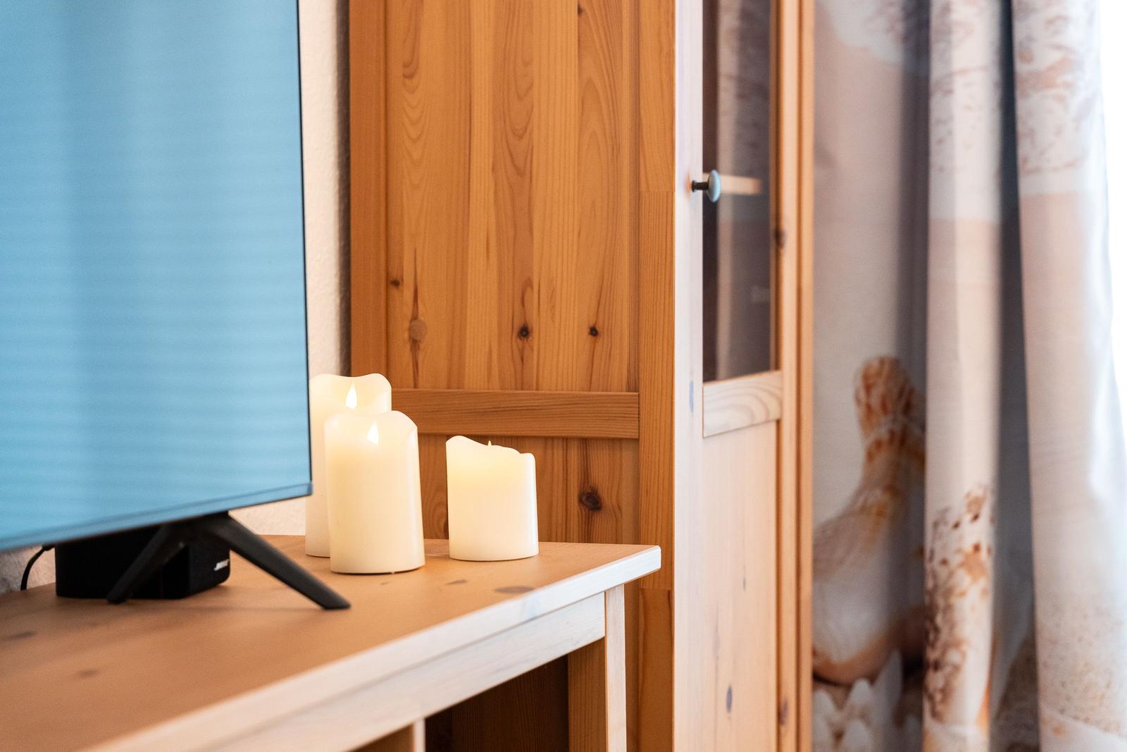 A TV sits on a table with three lit candles and a wooden cabinet behind it.