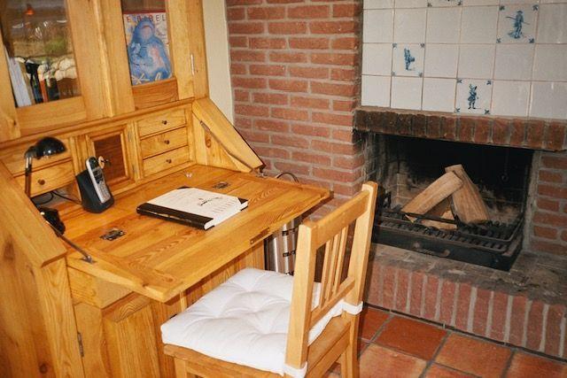 Holzschreibtisch mit Stuhl neben Kamin mit Backsteinwand und Fliesen.