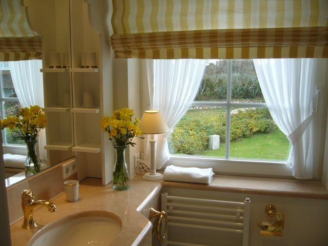 Badezimmer mit Fenster, gelb-weißem Rolladen und Blumen in Vasen.