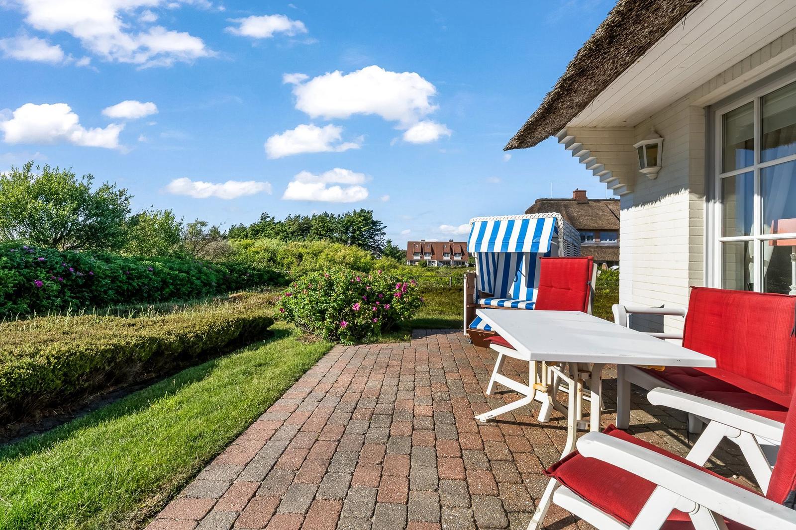 Terrasse mit Tisch, Stühlen und Strandkorb. Blick auf Grünflächen und Himmel.