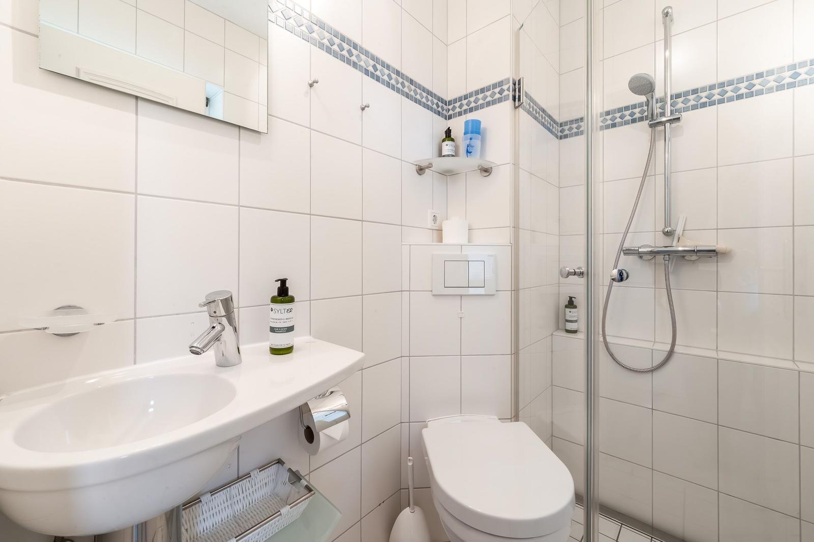 Badezimmer mit Dusche, Toilette und Waschbecken mit Spiegel.