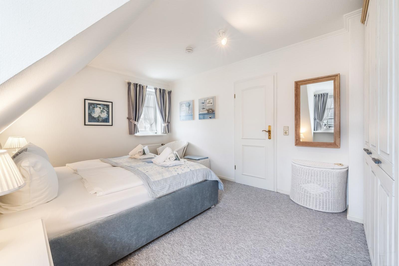 Schlafzimmer mit Dachschräge, Bett, Fenster, Spiegel und Schrank.