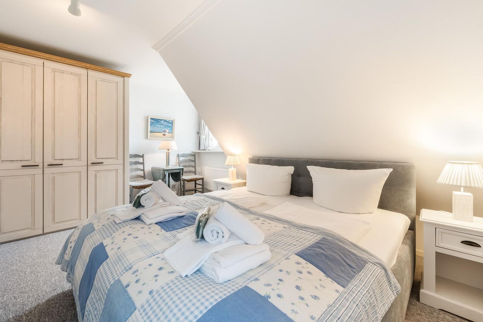 Schlafzimmer mit Doppelbett, Kleiderschrank und Nachttischen. Dachgeschoss mit schrägem Dach.