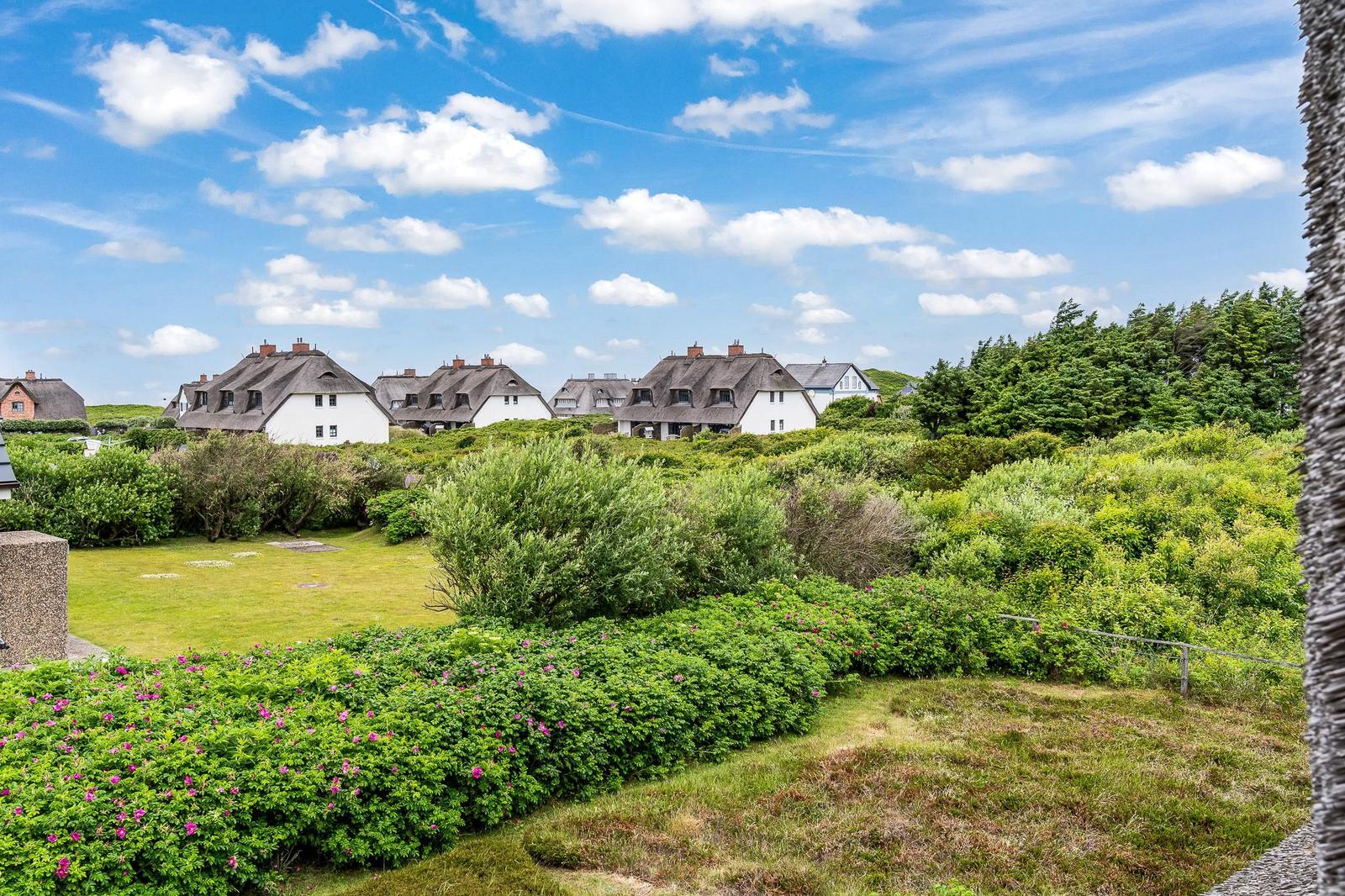 Weitläufiger Garten mit Blumenhecken und Blick auf traditionelle Häuser mit Dachziegeln.