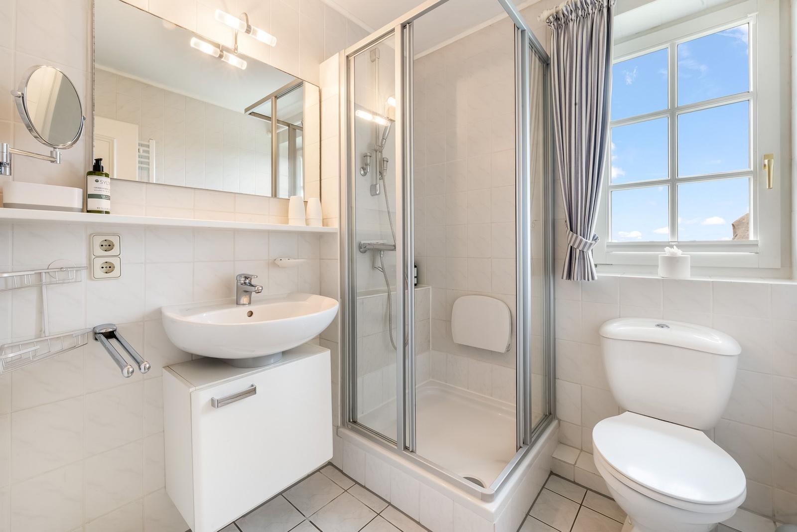 Badezimmer mit Dusche, Waschbecken und Toilette. Fenster mit Blick auf Himmel.