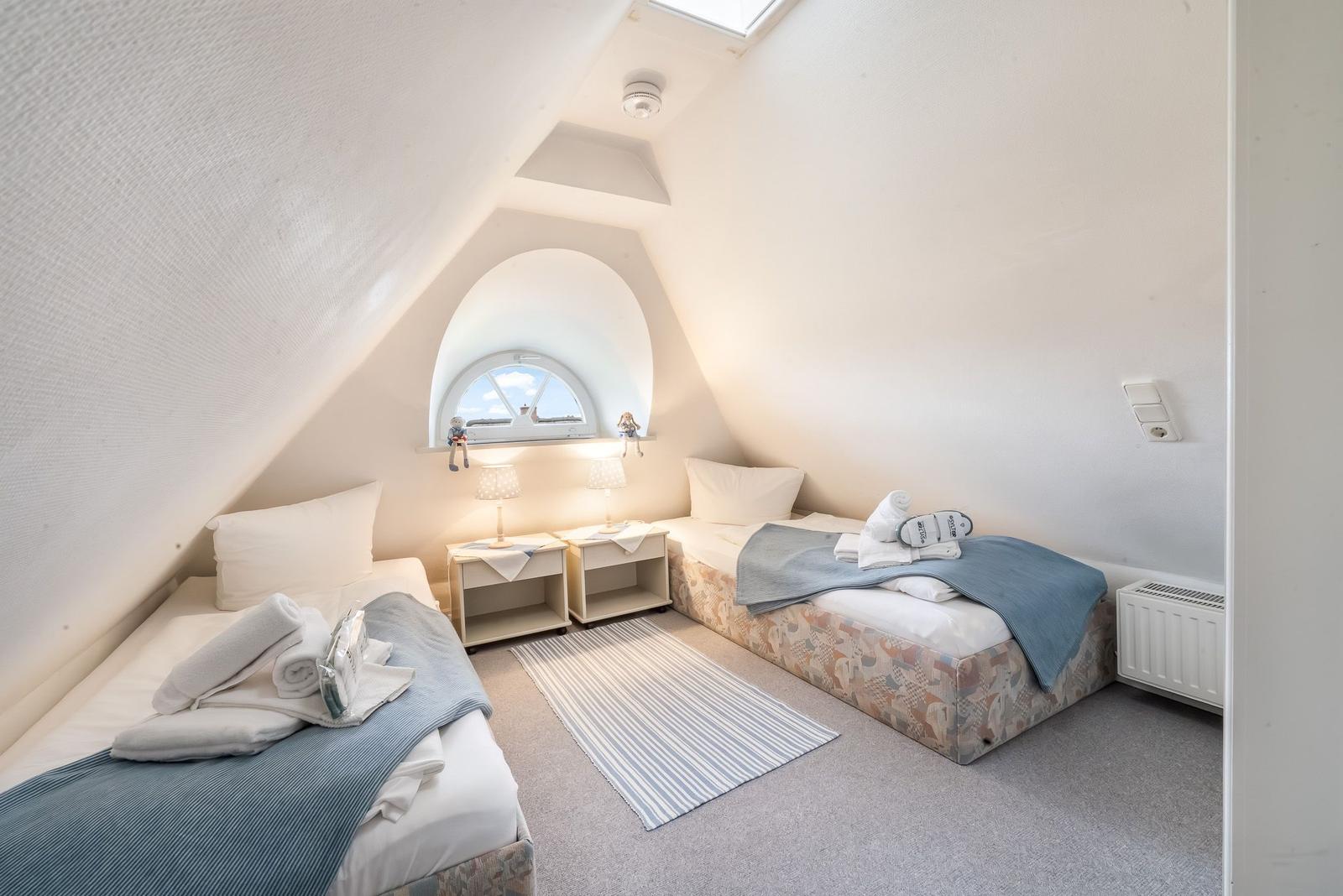 Zwei Betten in einem Dachzimmer mit Fenster und Nachttischen.