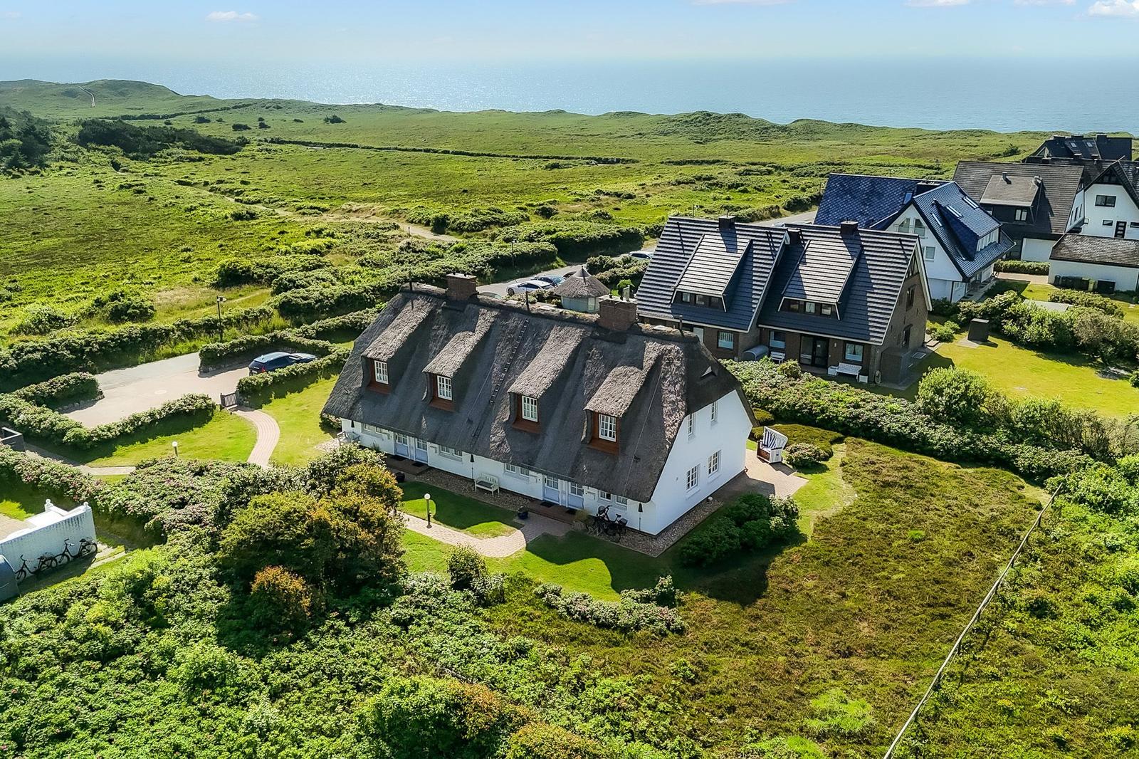 Haus mit strohgedecktem Dach, umgeben von Grünland und Meer.