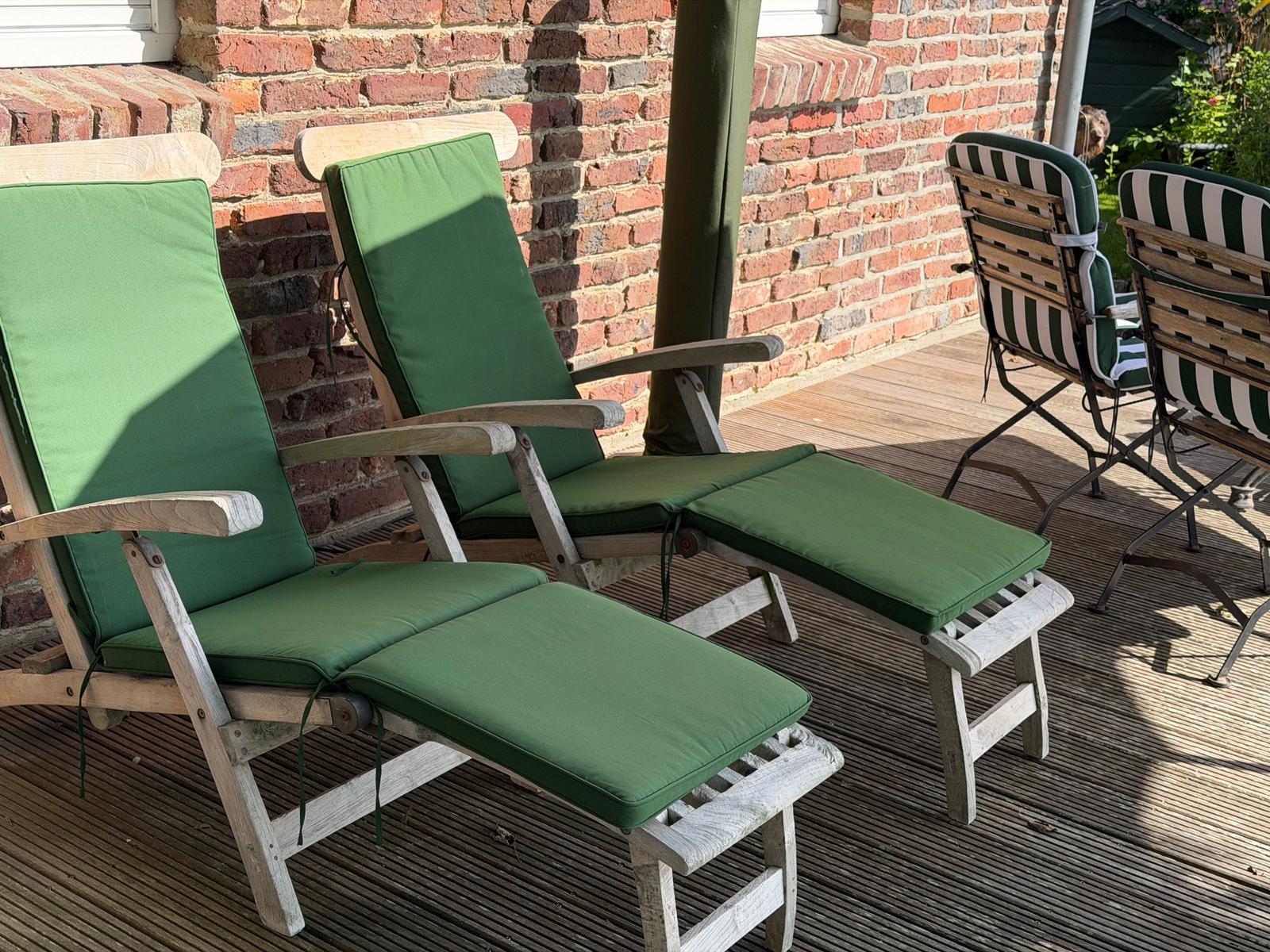Zwei grüne Liegestühle mit Fußstützen stehen auf einer Holterrasse vor einer Backsteinmauer.