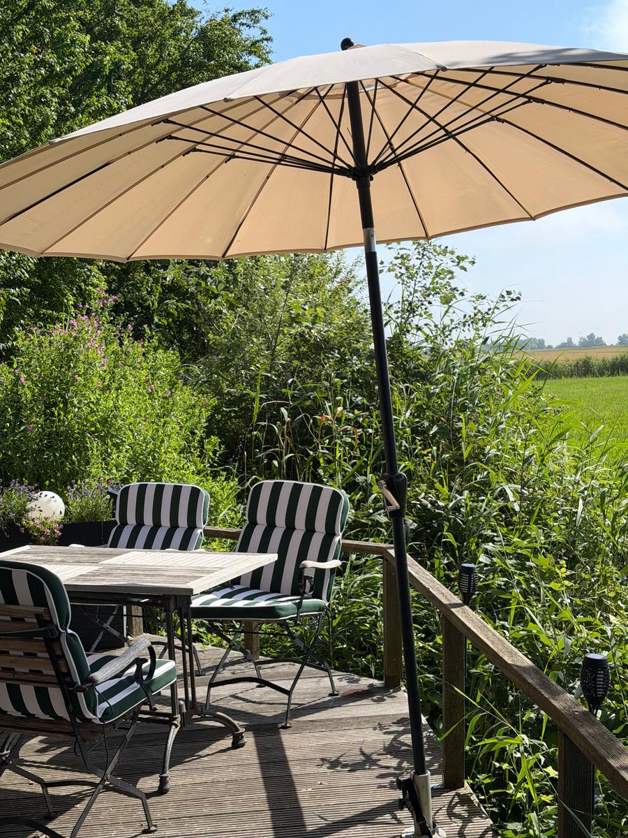 Terrasse mit Tisch, Stühlen und Sonnenschirm. Blick auf grüne Wiesen und Bäume.