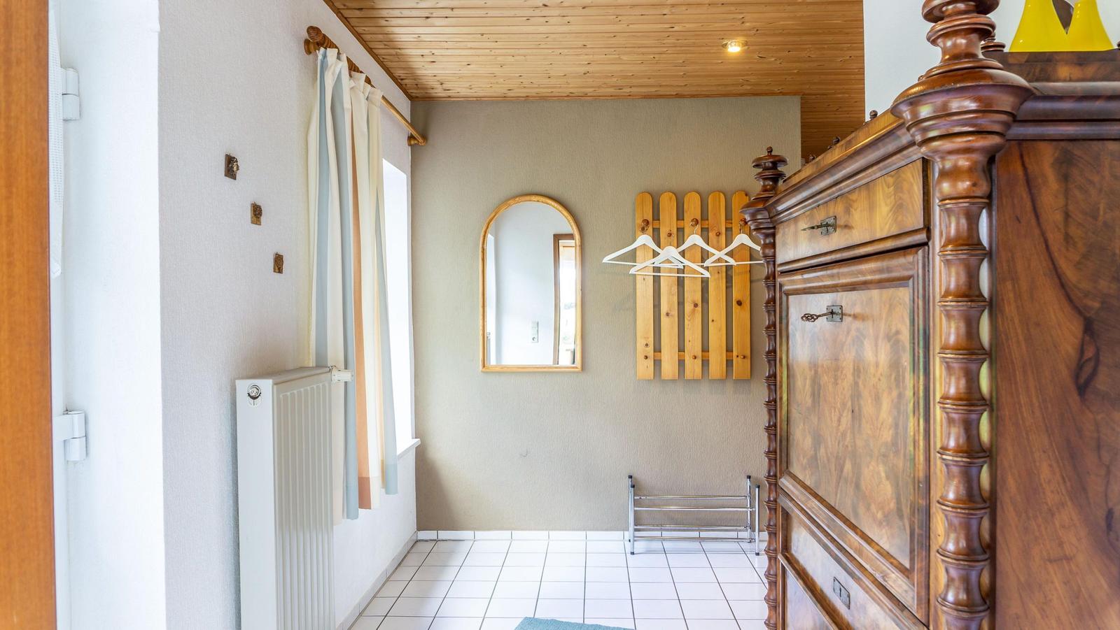 Schlafzimmer mit Holzboden, Spiegel, Kleiderständer und Holzschnitzereien an der Wand.