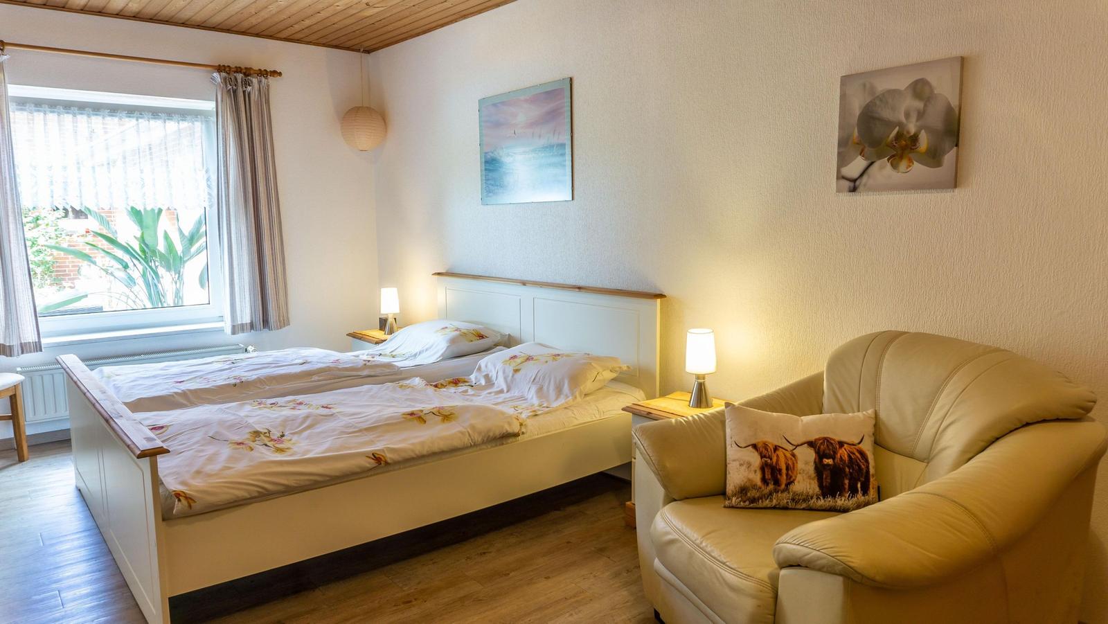 Schlafzimmer mit Doppelbett, Sessel und Fenster mit Blick auf Garten.