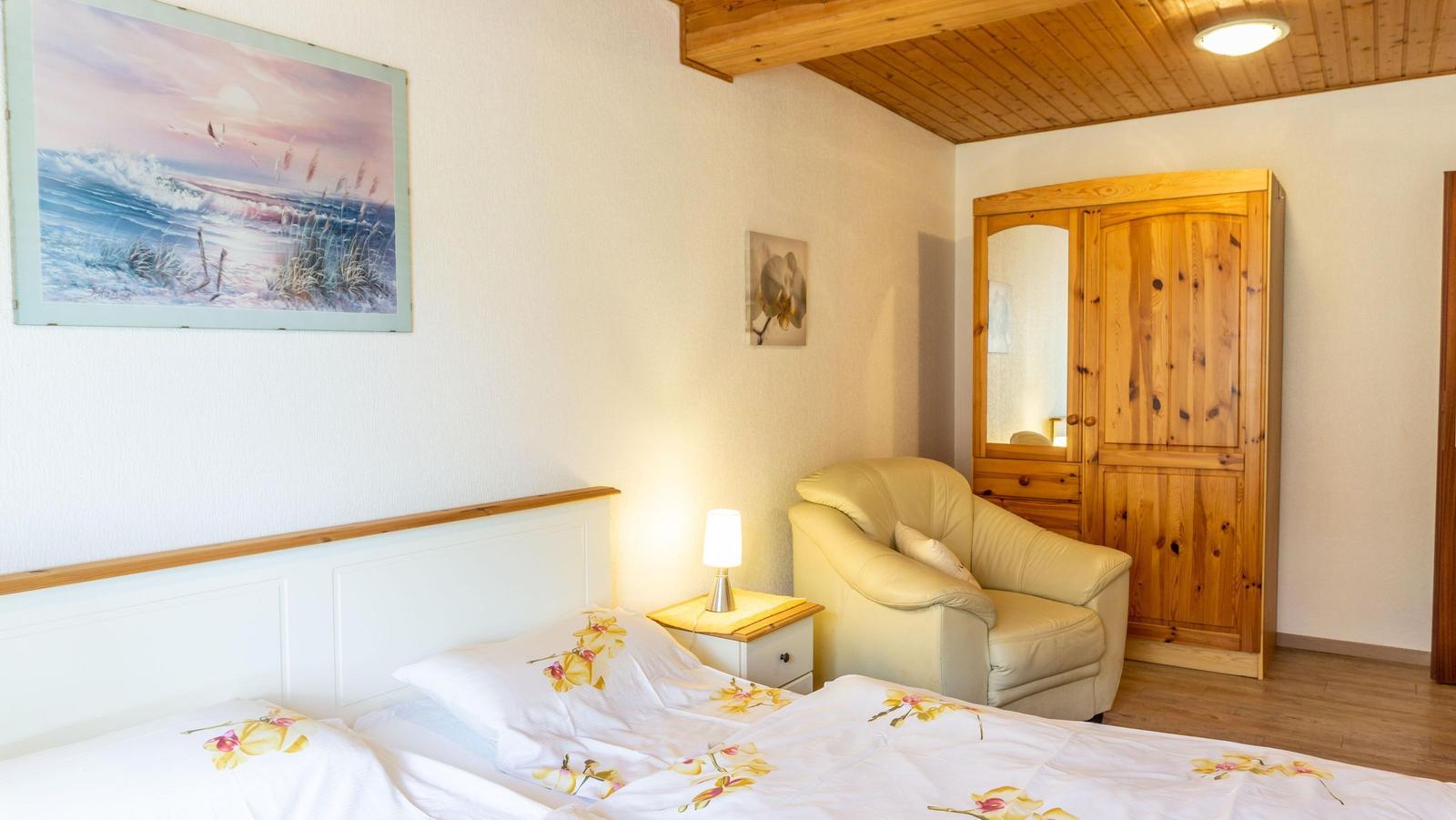 Schlafzimmer mit Bett, Sessel, Kleiderschrank und Wandbild.