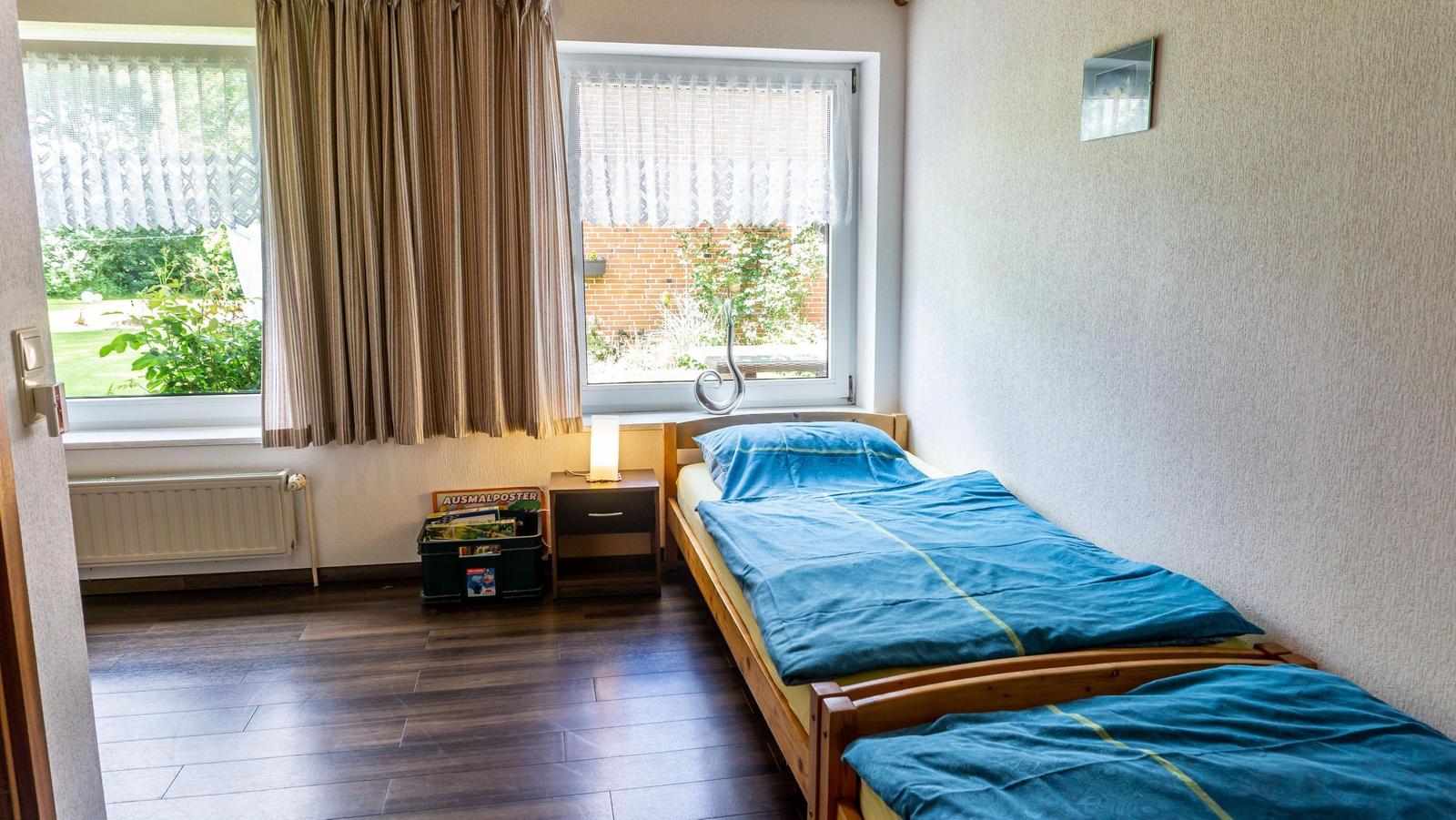 Zimmer mit zwei Einzelbetten, Holzboden und Fenstern zum Garten.