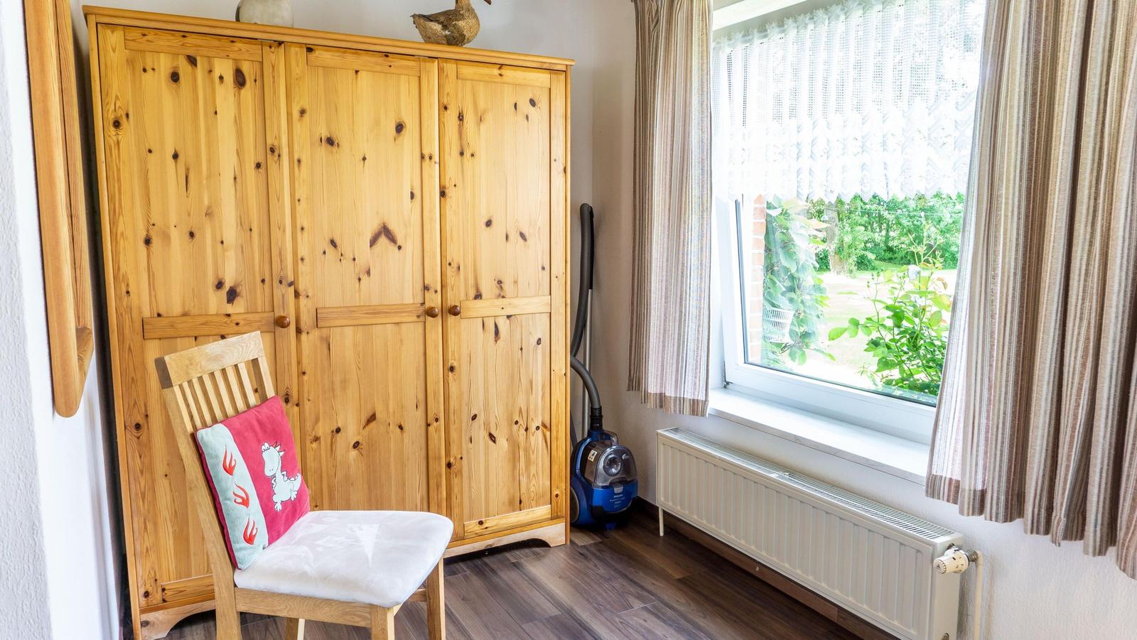 Ein Raum mit Holzschrank, Stuhl und Fenster mit Blick auf Garten.