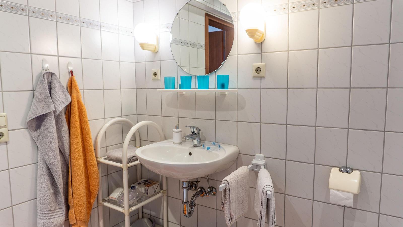 Badezimmer mit Waschbecken, Spiegel, Handtüchern und Toilettenpapierhalter.