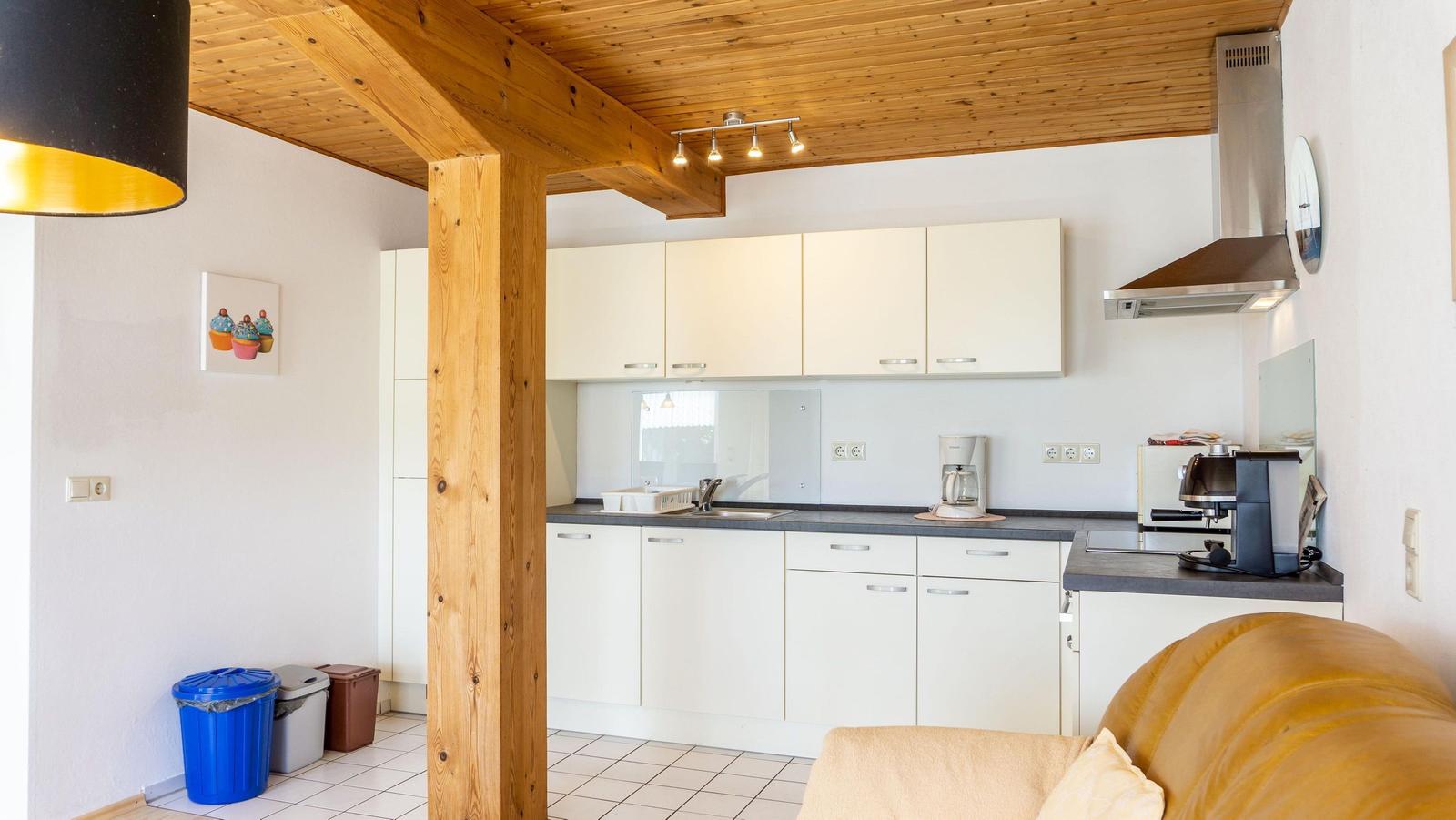 Küche mit weißen Schränken, Edelstahlherd und Holzdecke mit Balken.