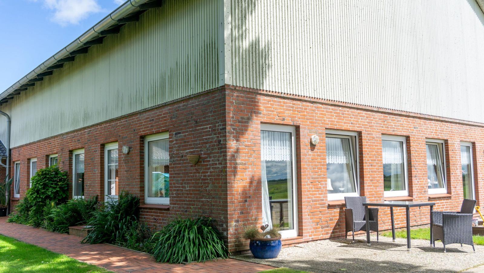 Haus mit Backsteinfassade und Terrasse mit Tisch und Stühlen.