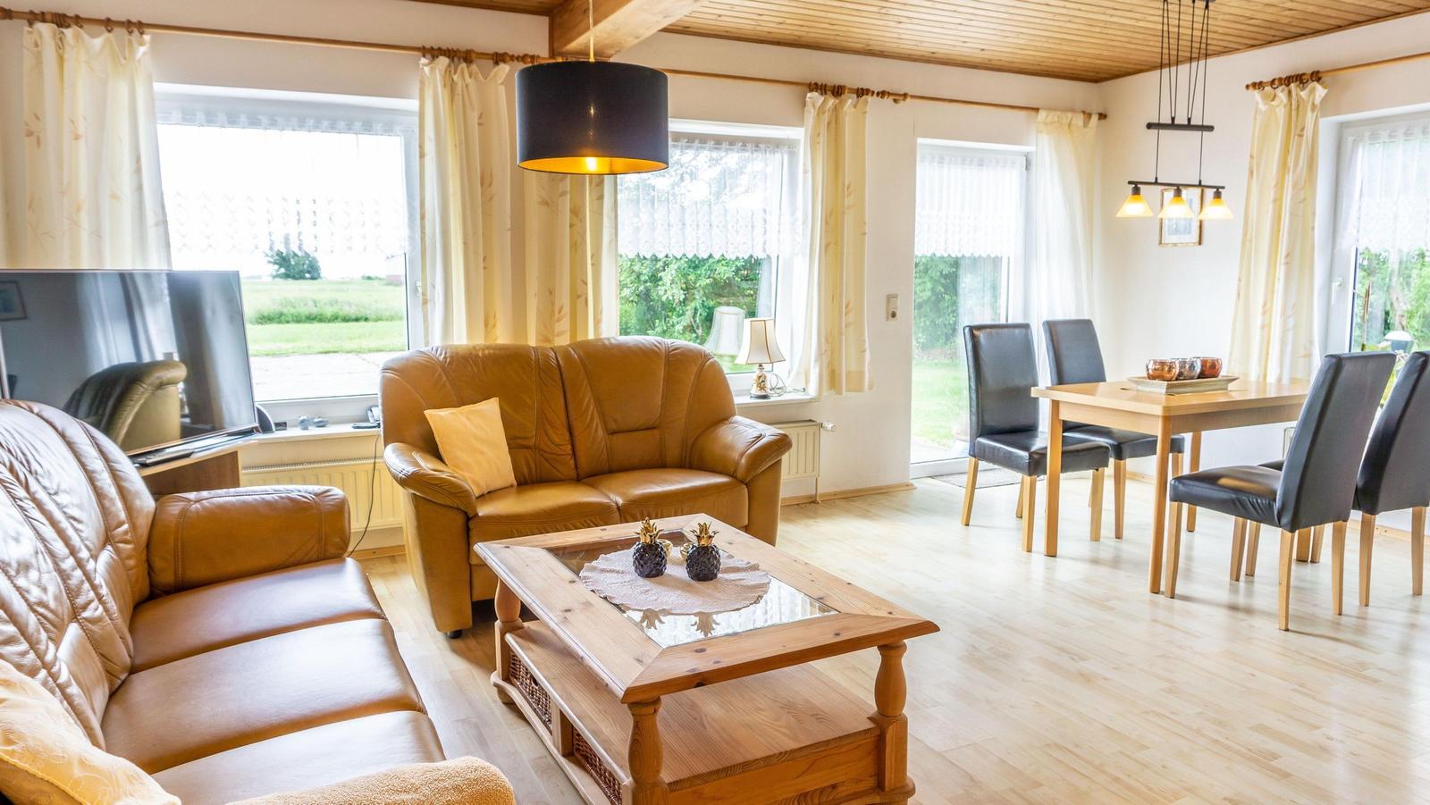 Wohn- und Essbereich mit Leder-Sofa, Holztisch und großen Fenstern.