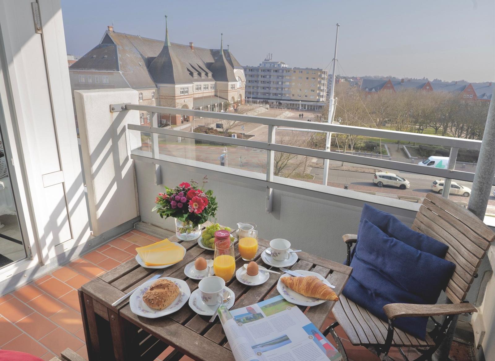 Balkon mit Tisch, Stuhl und Frühstück. Blick auf Gebäude und Straße.