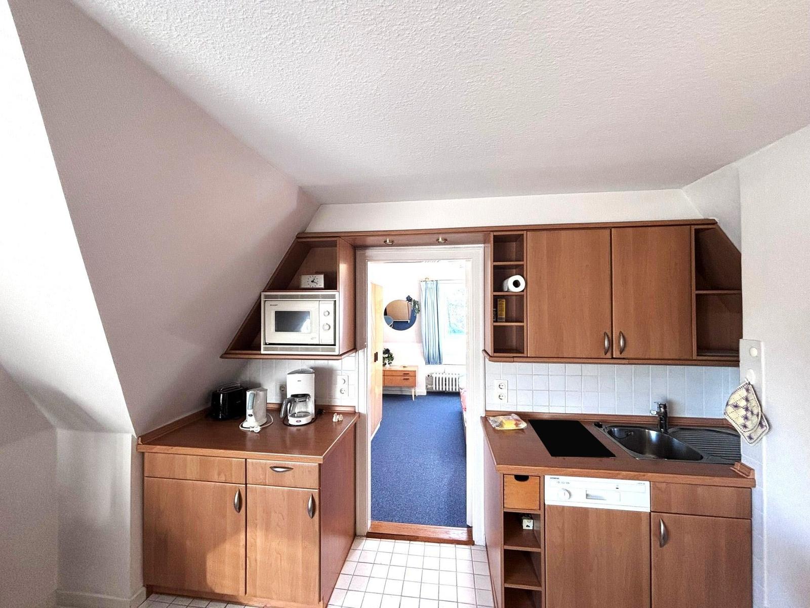 Kitchen with wooden cabinets, sink, and microwave. Passage to a room with blue carpet.