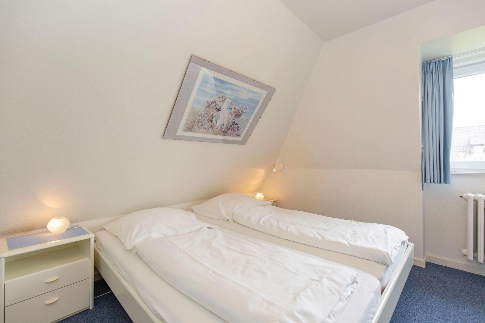 Bedroom with double bed, nightstand, and picture on the wall. Window with blue curtains.