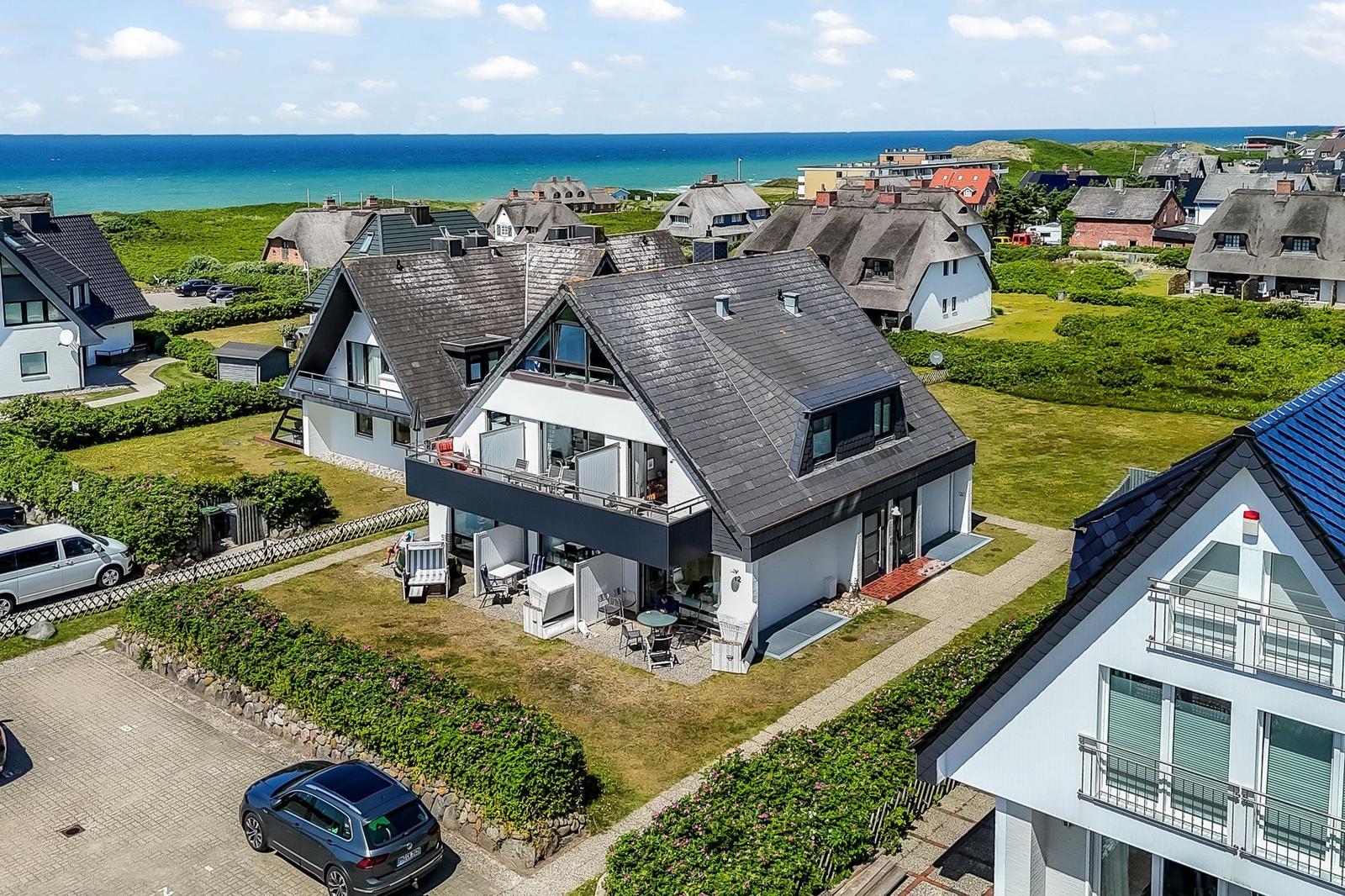Moderne Villa mit Terrasse und Blick auf das Meer. Umgeben von Grünflächen und anderen Häusern.