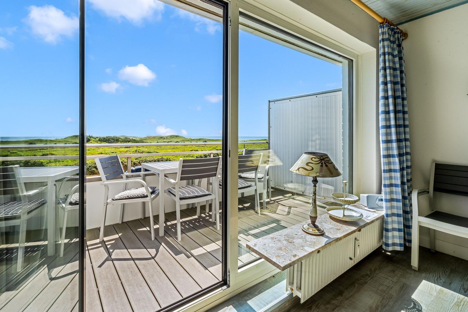 Terrasse mit Tisch und Stühlen, Blick auf Grünland und Meer.