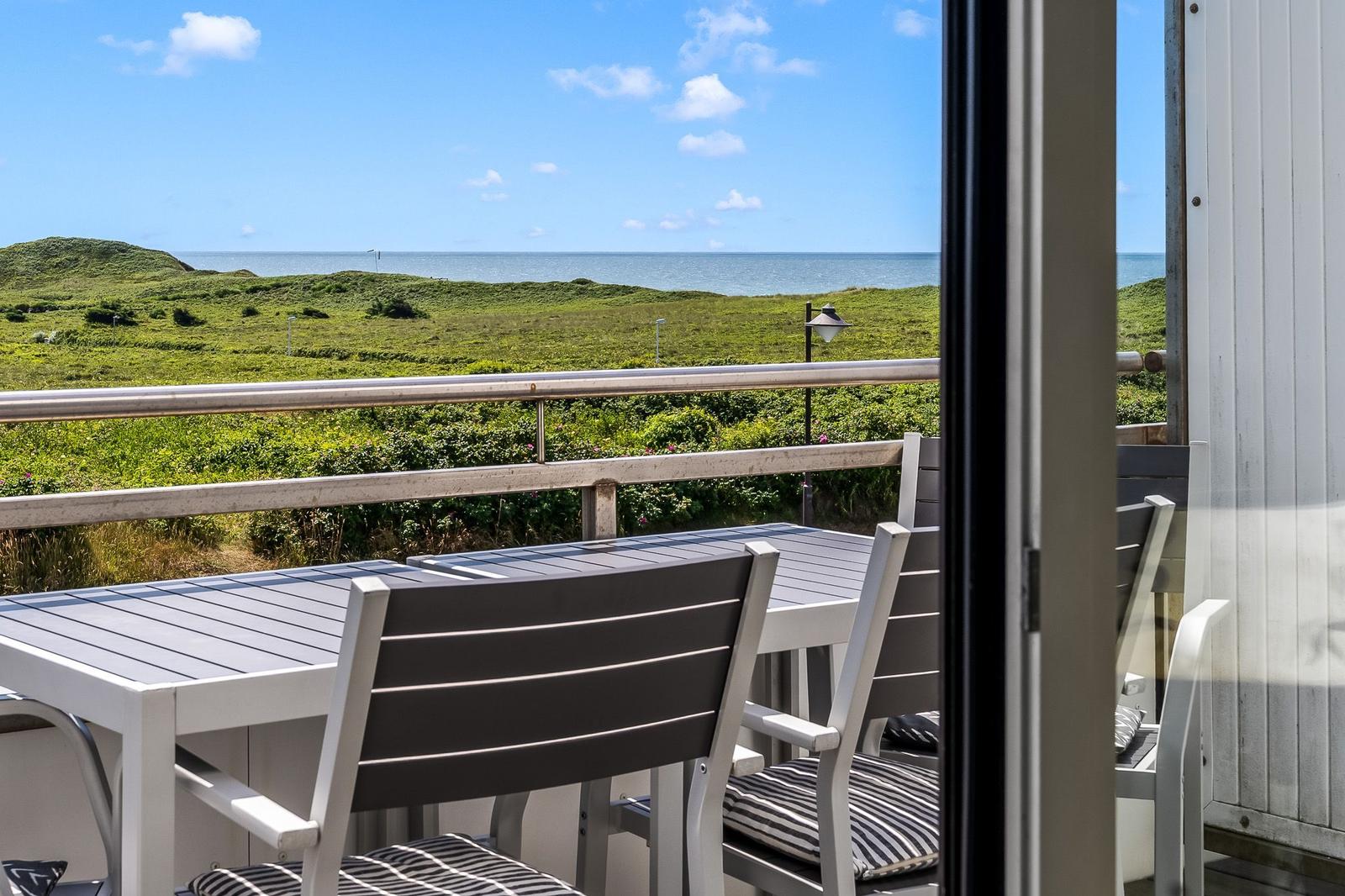 Terrasse mit Tisch und Stühlen, Blick auf grüne Wiesen und Meer.