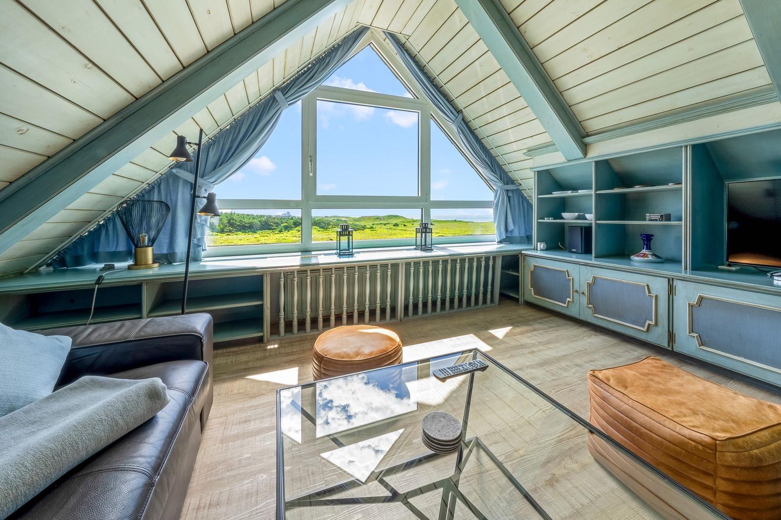 Dachgeschosswohnung mit großem Fenster, Sofa, Couchtisch und integriertem Schrank.
