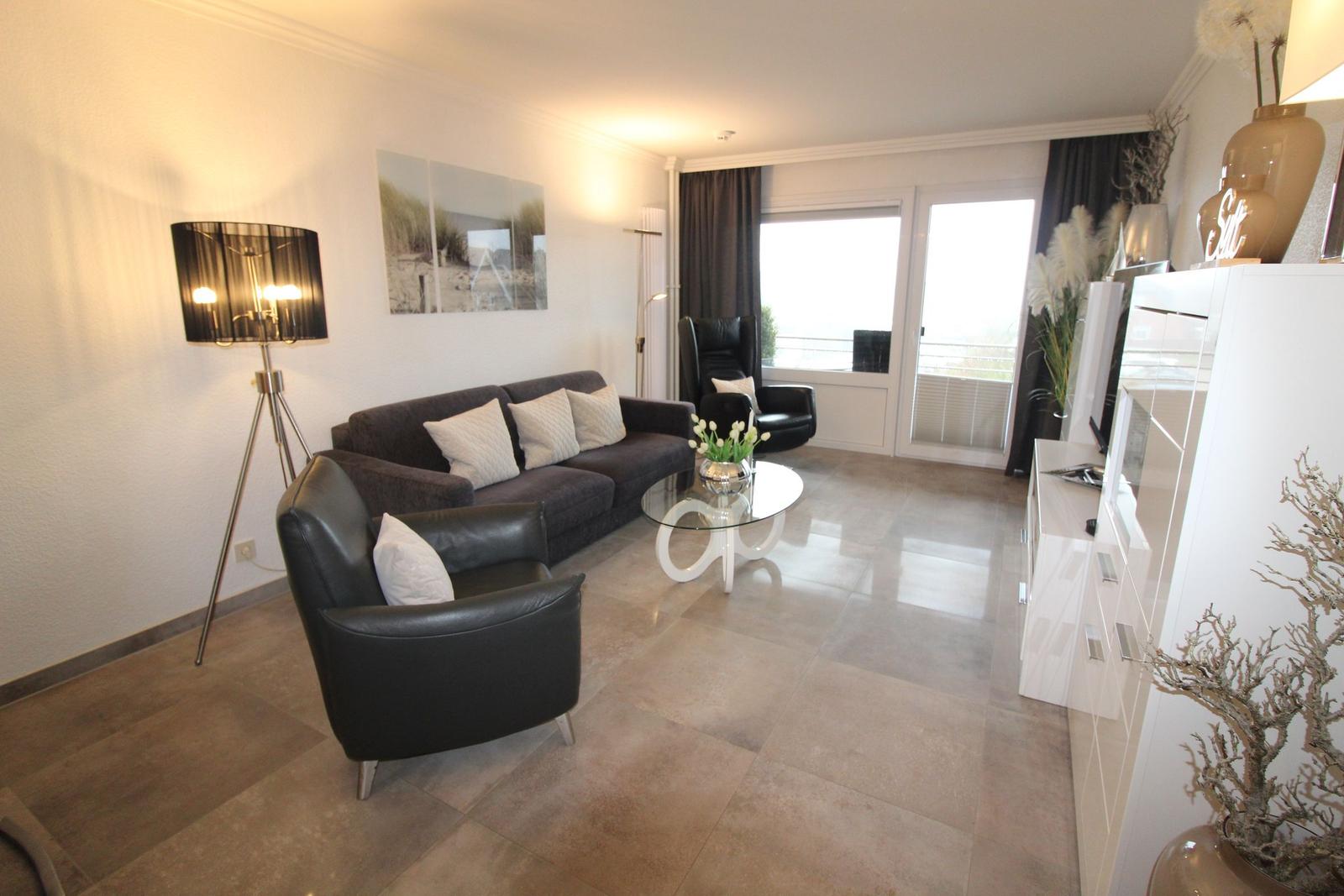 Living room with sofa, chairs, and glass table. Terrace with view. White furnishings.