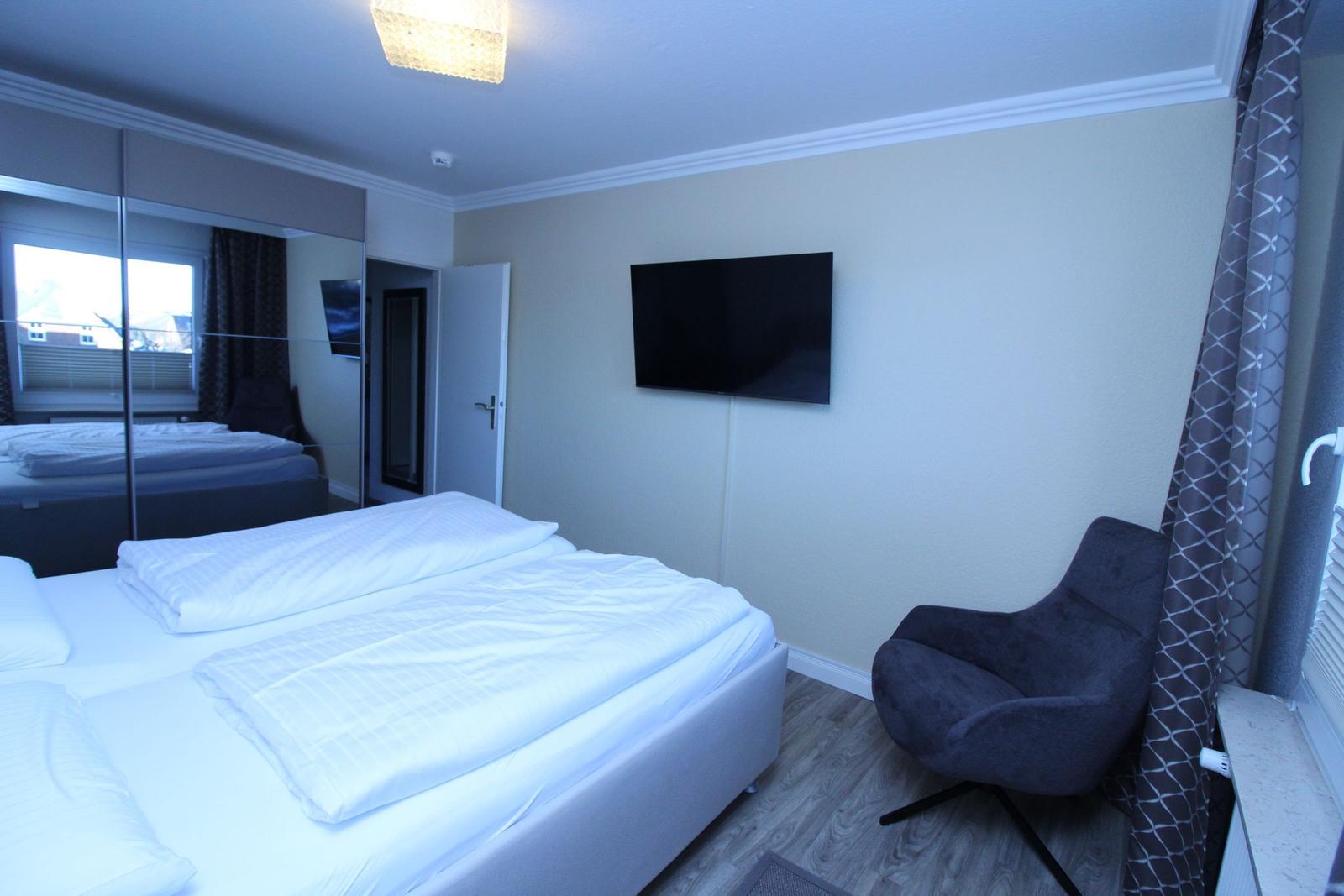 Bedroom with double bed, TV, and armchair.
