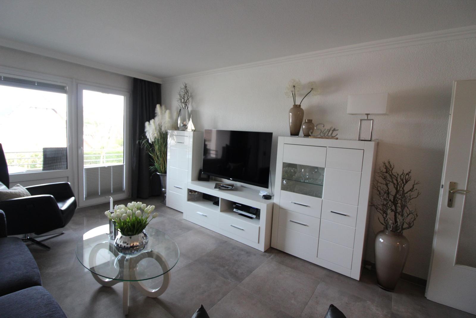 Living room with TV, glass table, and white cabinets. Doorway and balcony door visible.