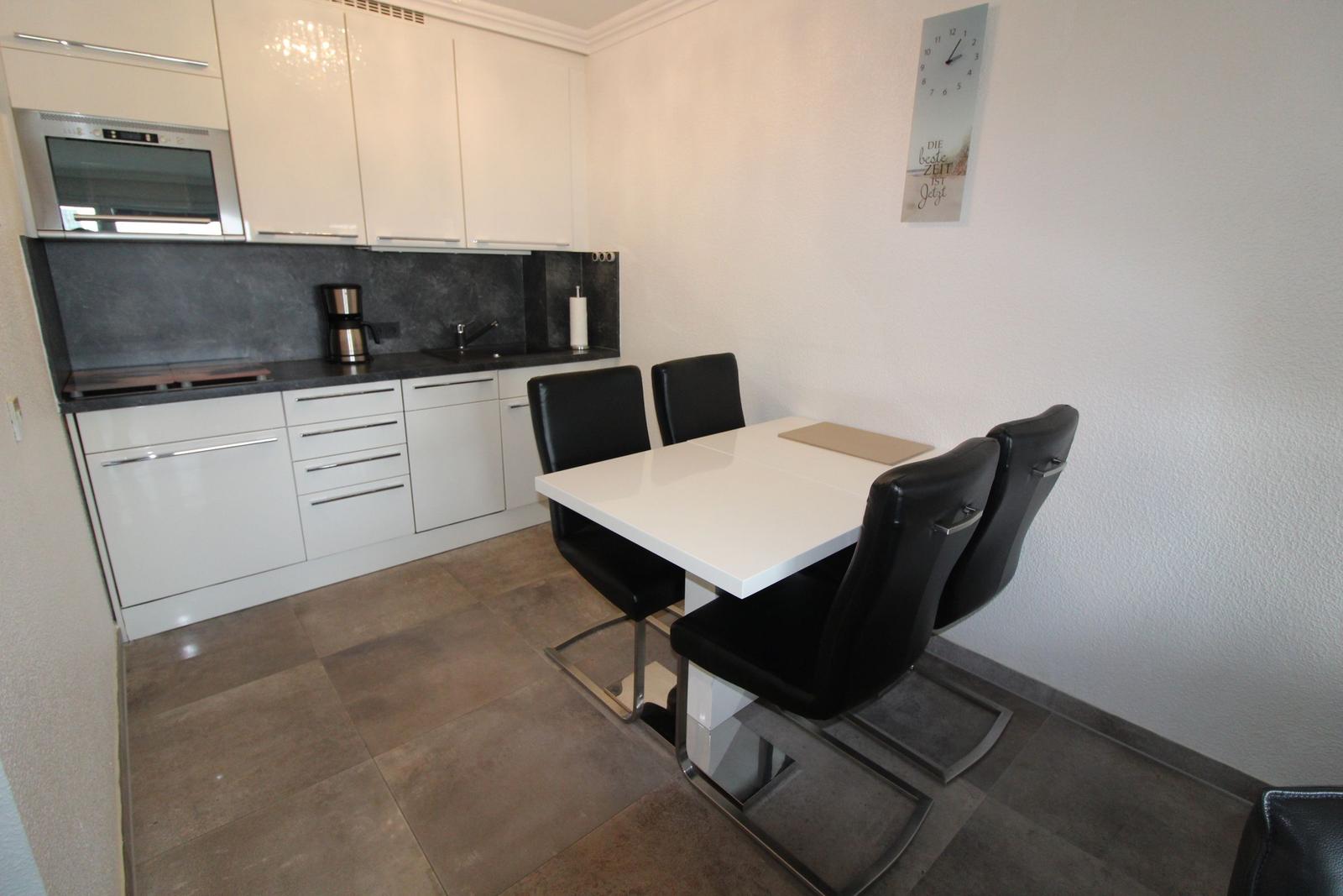 Kitchen with dining area, white countertop, black chairs, and wall clock.