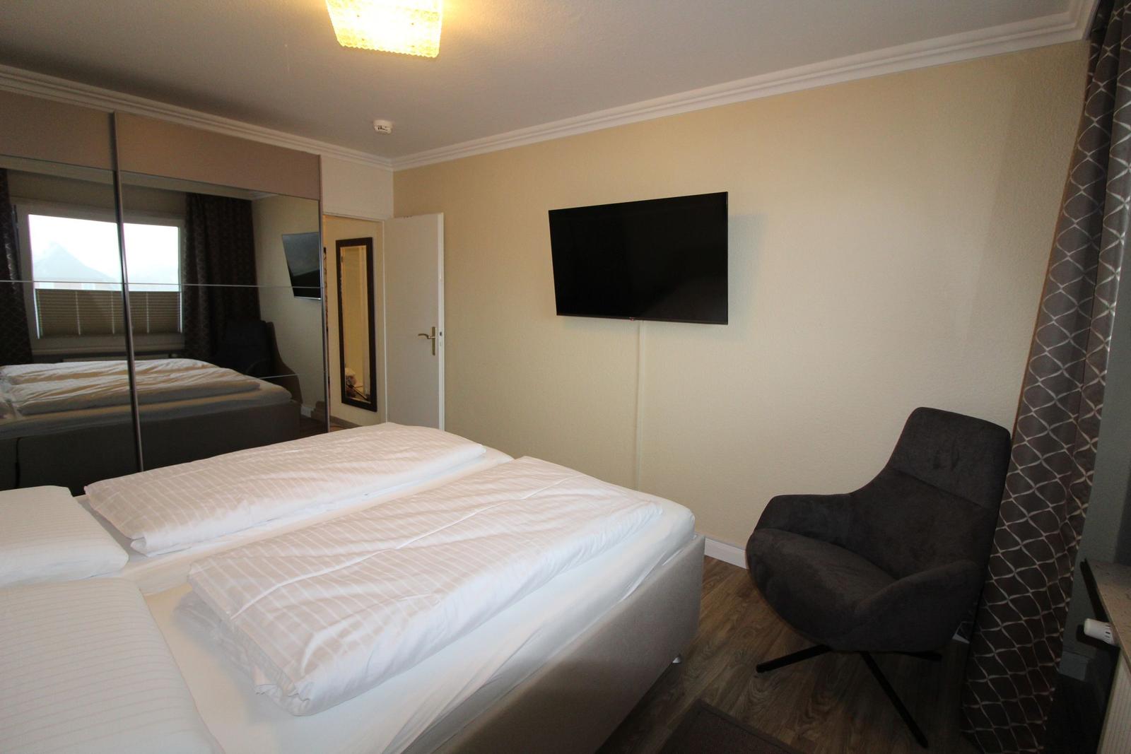 Bedroom with double bed, wall-mounted TV, and armchair.