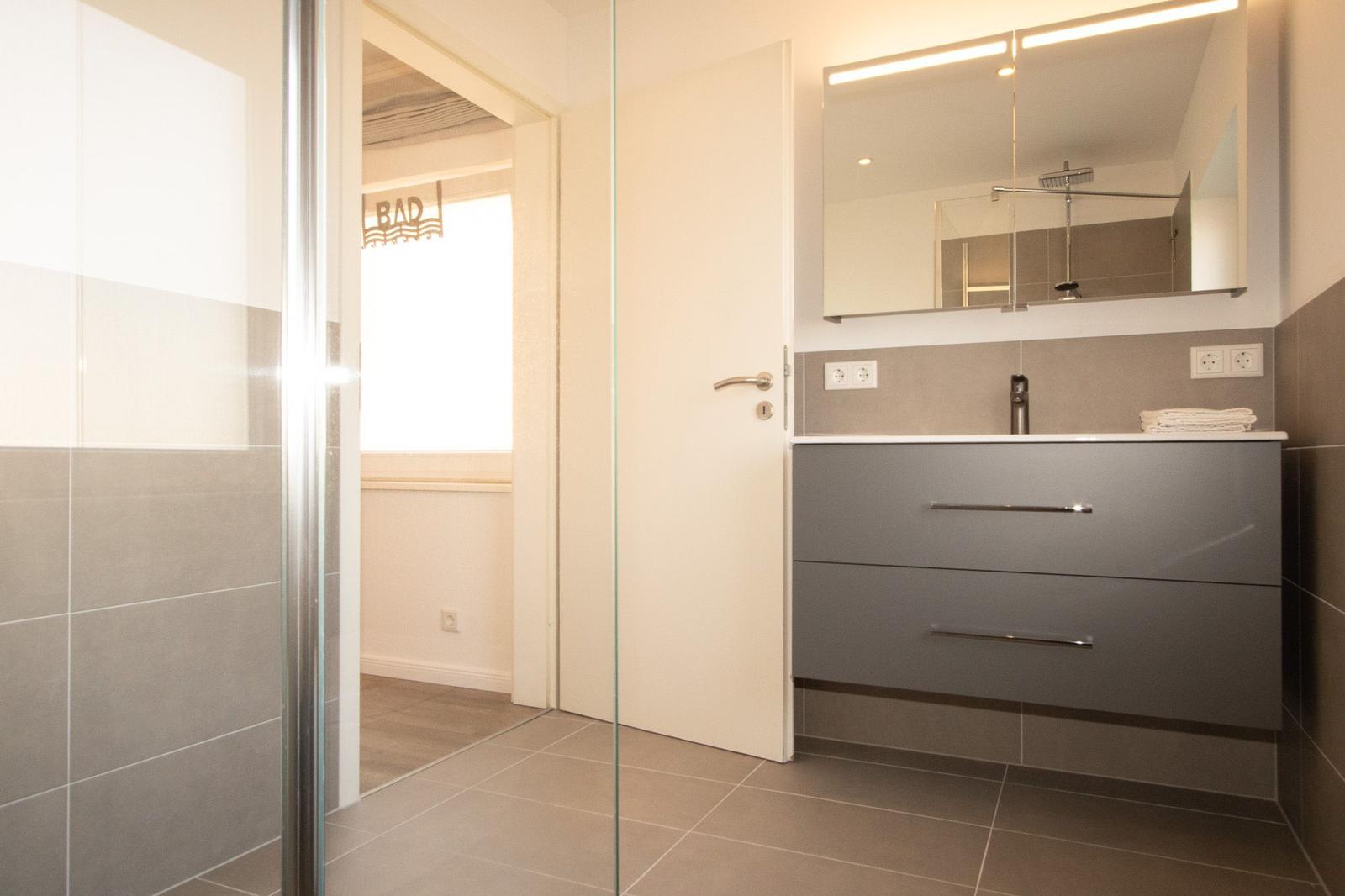 Badezimmer mit Glasdusche, Waschtisch und Spiegel