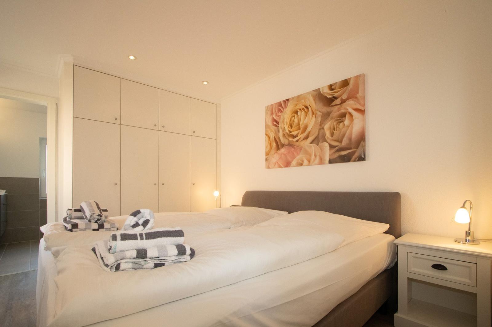 Schlafzimmer mit Doppelbett, Kleiderschrank und Wandbild mit Rosen.