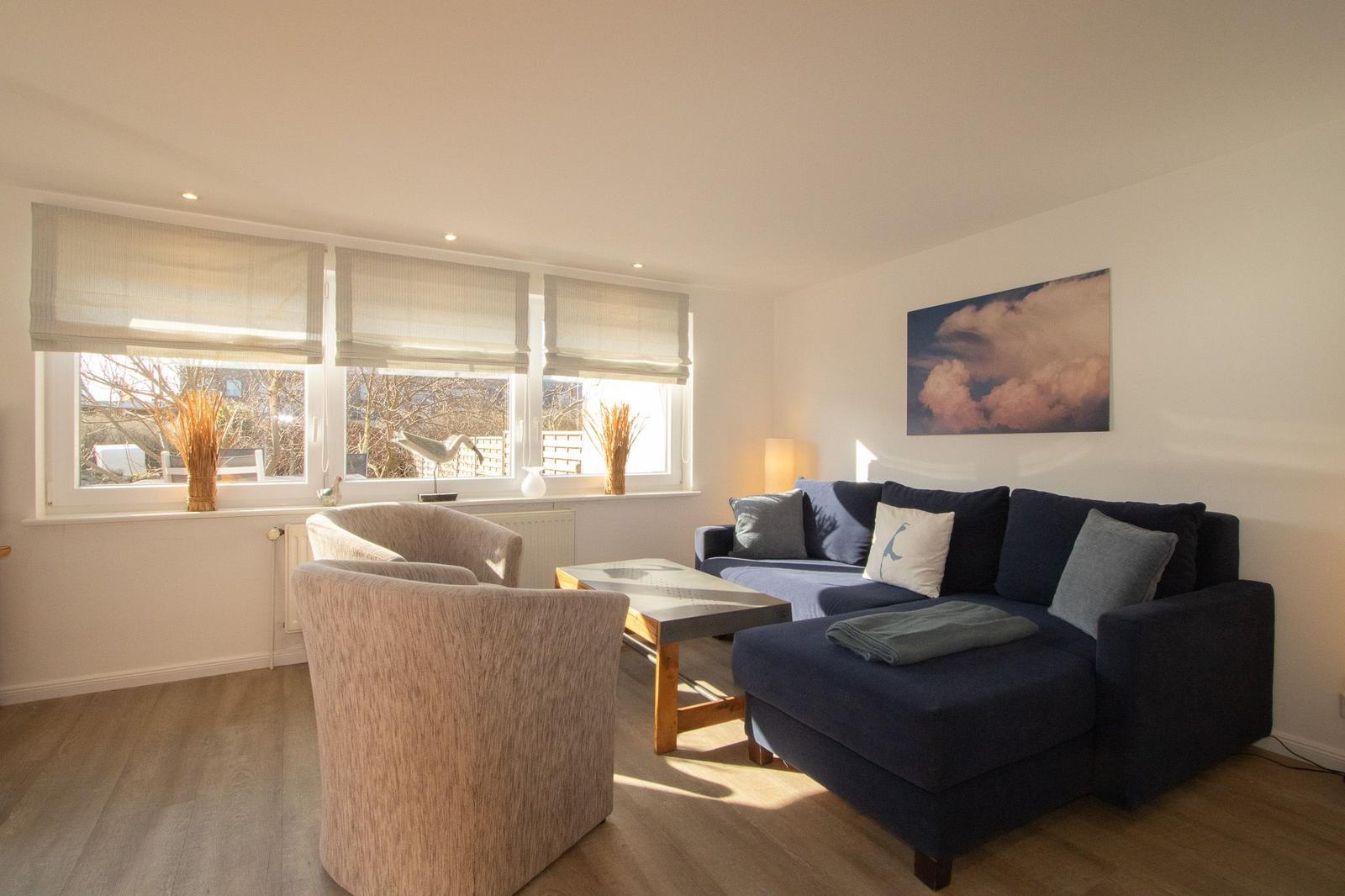 Ein Wohnzimmer mit einem dunkelblauen Sofa, zwei Sesseln und einem Tisch. An der Wand hängt ein Bild.
