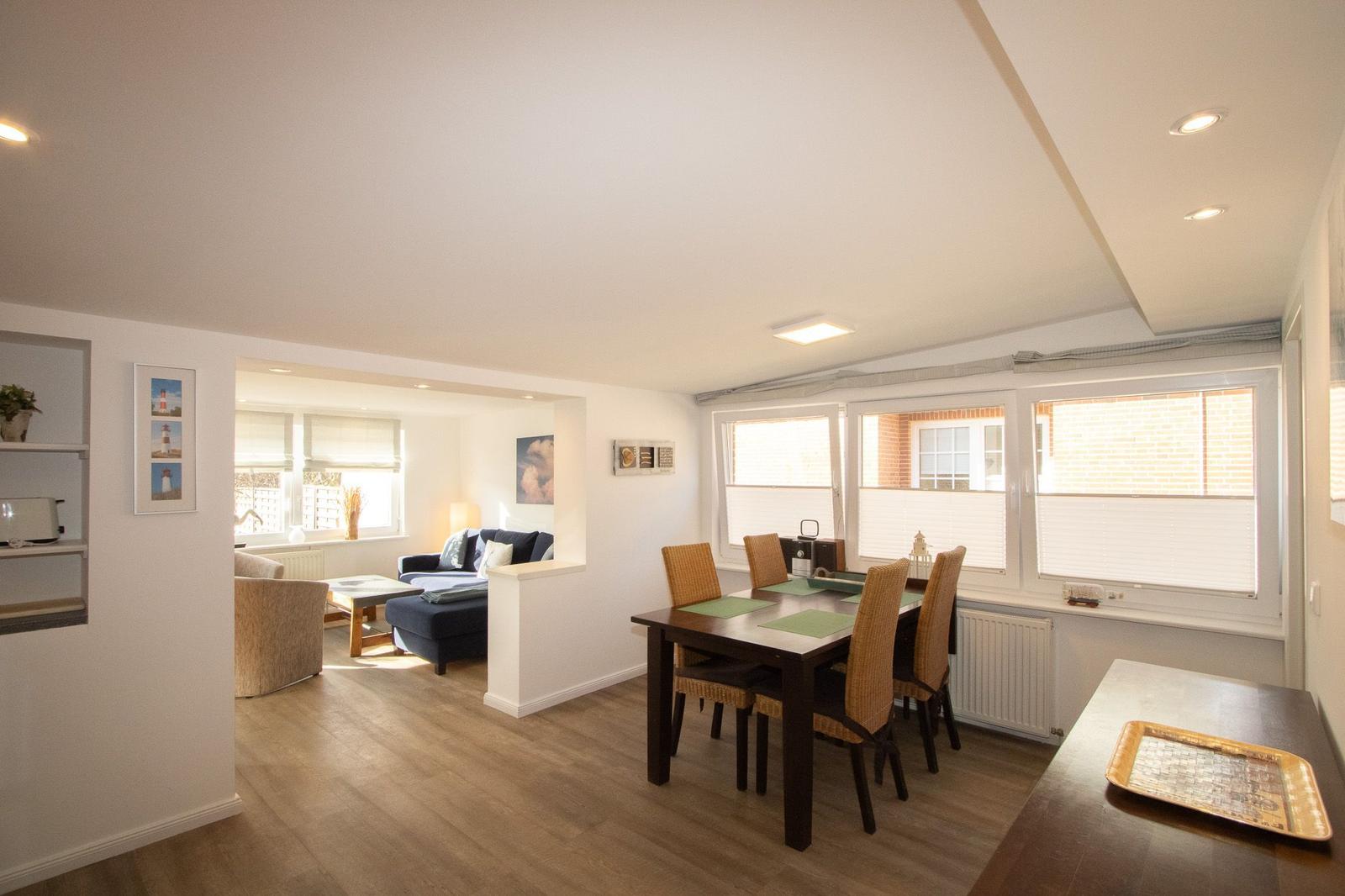 Wohn- und Essbereich mit Tisch, Stühlen und Fenstern. Wohnzimmer mit Sofa und Couchtisch.