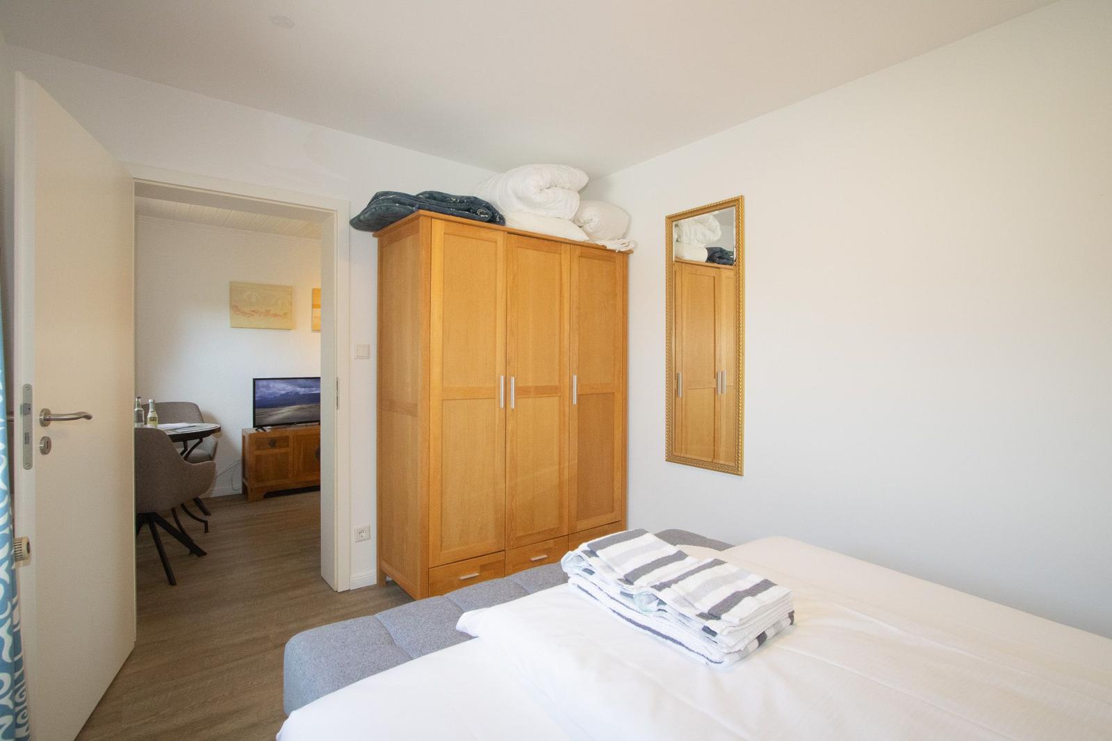 Bedroom with bed, wardrobe, and mirror. Passage to living area with TV.