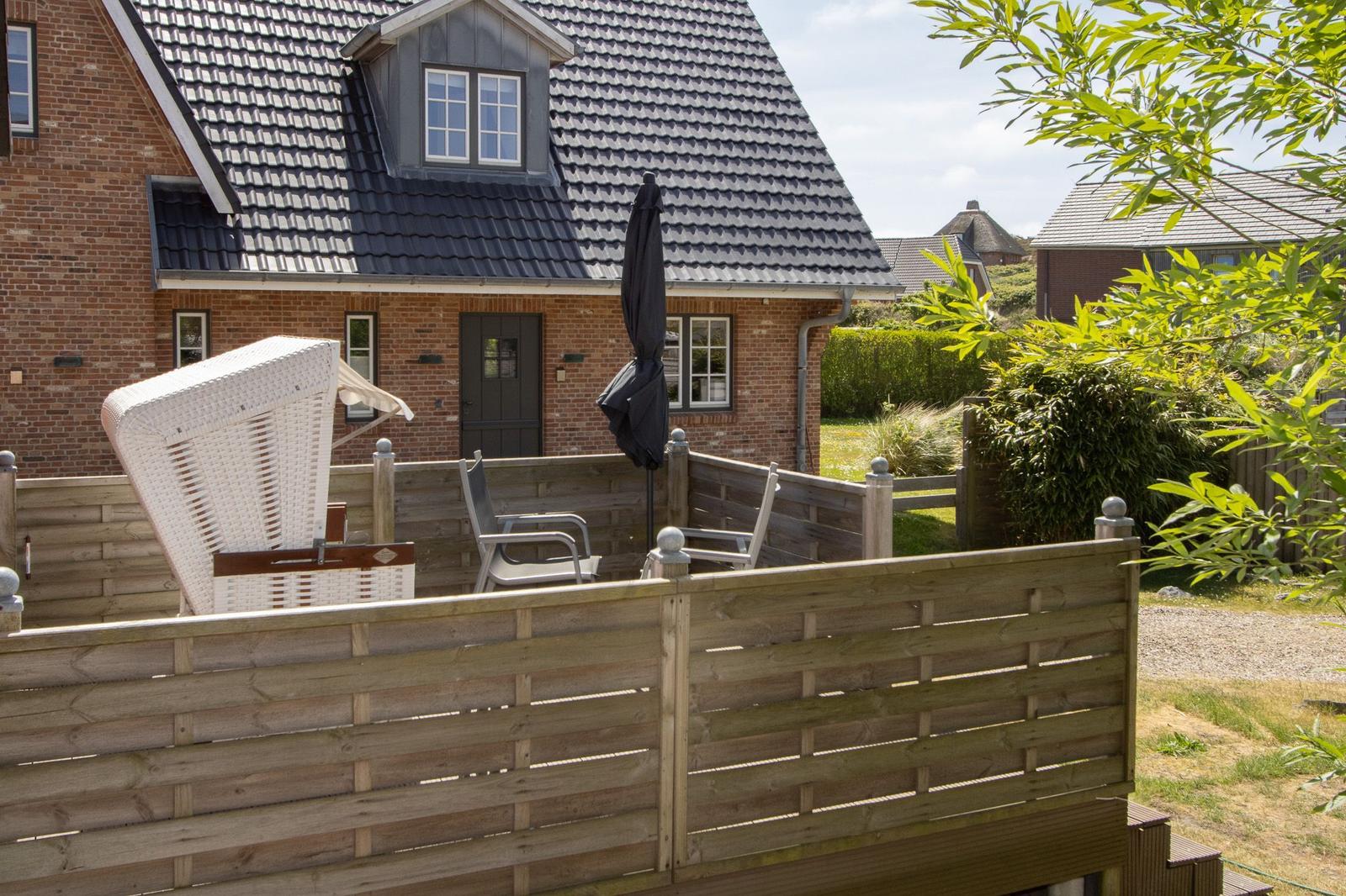 Terrace with lounge chair and umbrella in front of a brick house.