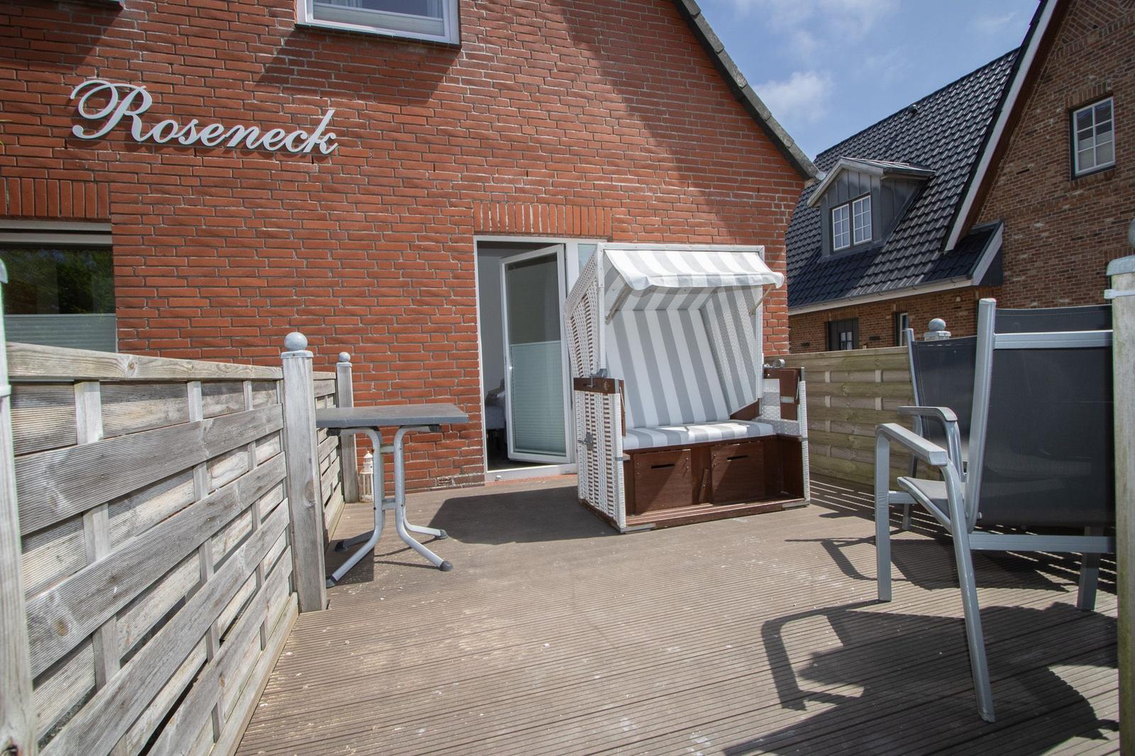 Terrace with beach chair, table and chair in front of red brick house with sign Roseneck.