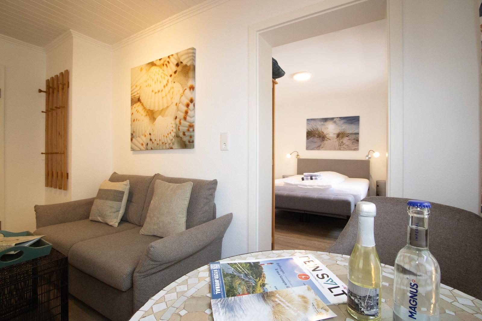 Living area with sofa and table. Bedroom with bed is visible in the background.