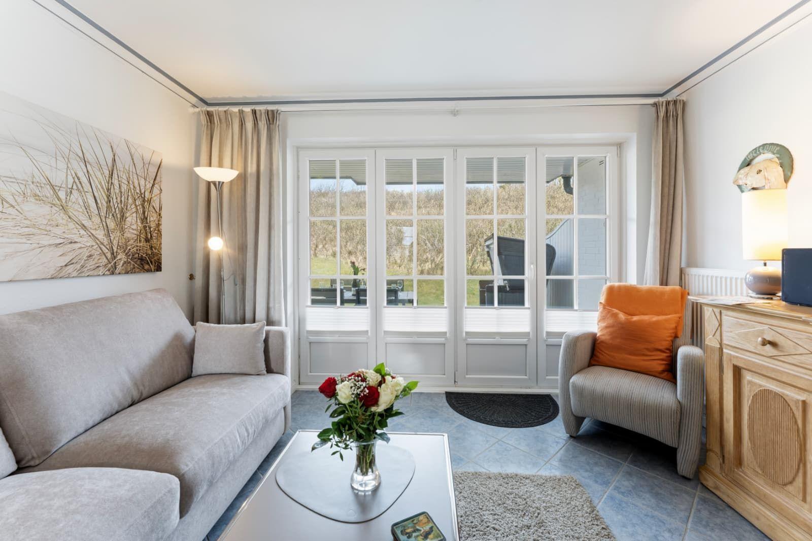 Wohnzimmer mit Sofa, Sessel und Glastüren zum Garten.